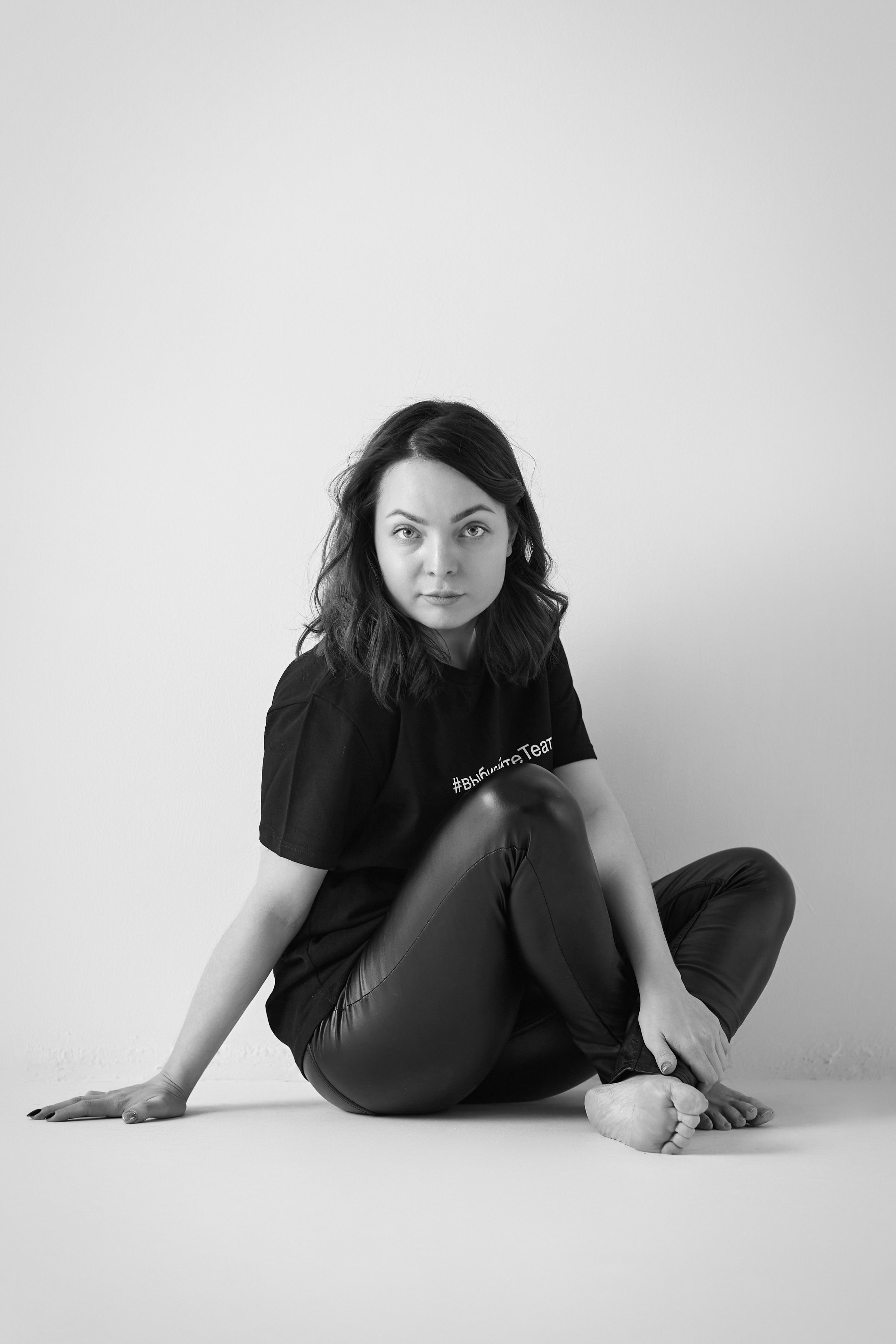 Темноволосая модель Татьяна находится на стуле в светлом платье на фоне светлой стены в студии.