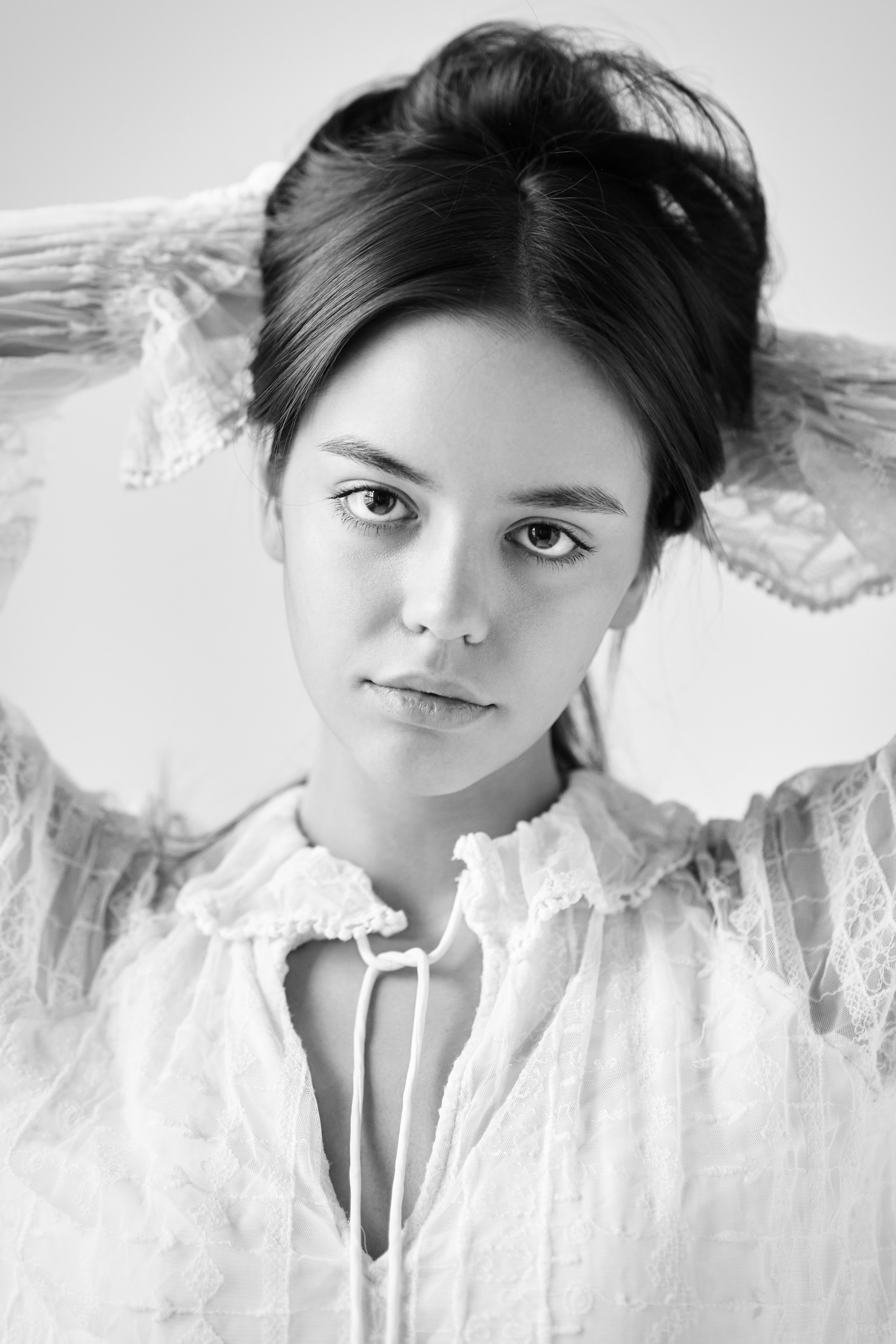 На светлом фоне в студии стоит модель Амина в светлом платье, ее волосы свободно лежат на спине.