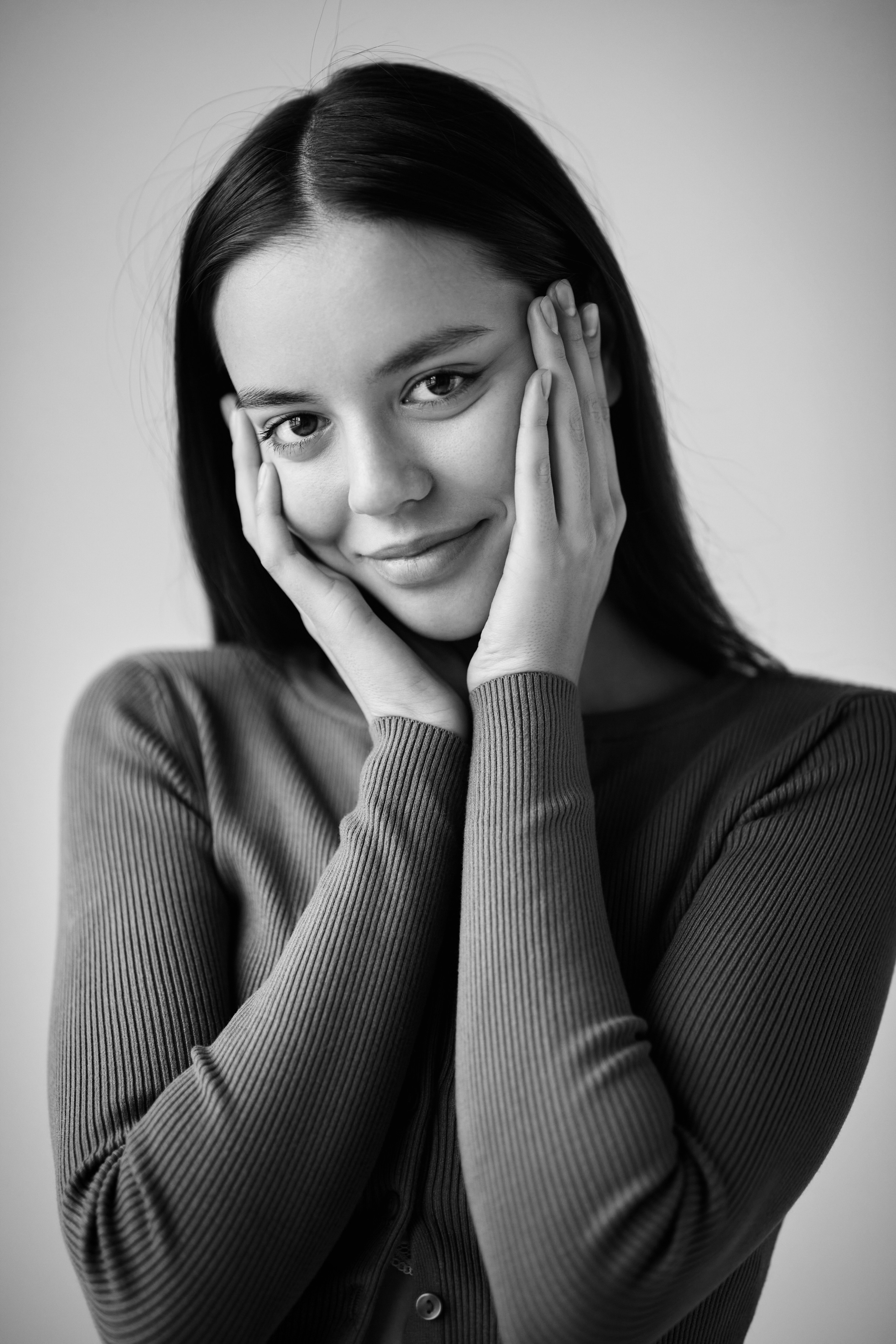 На светлом фоне темноволосая модель Амина в белом топике и джинсах.