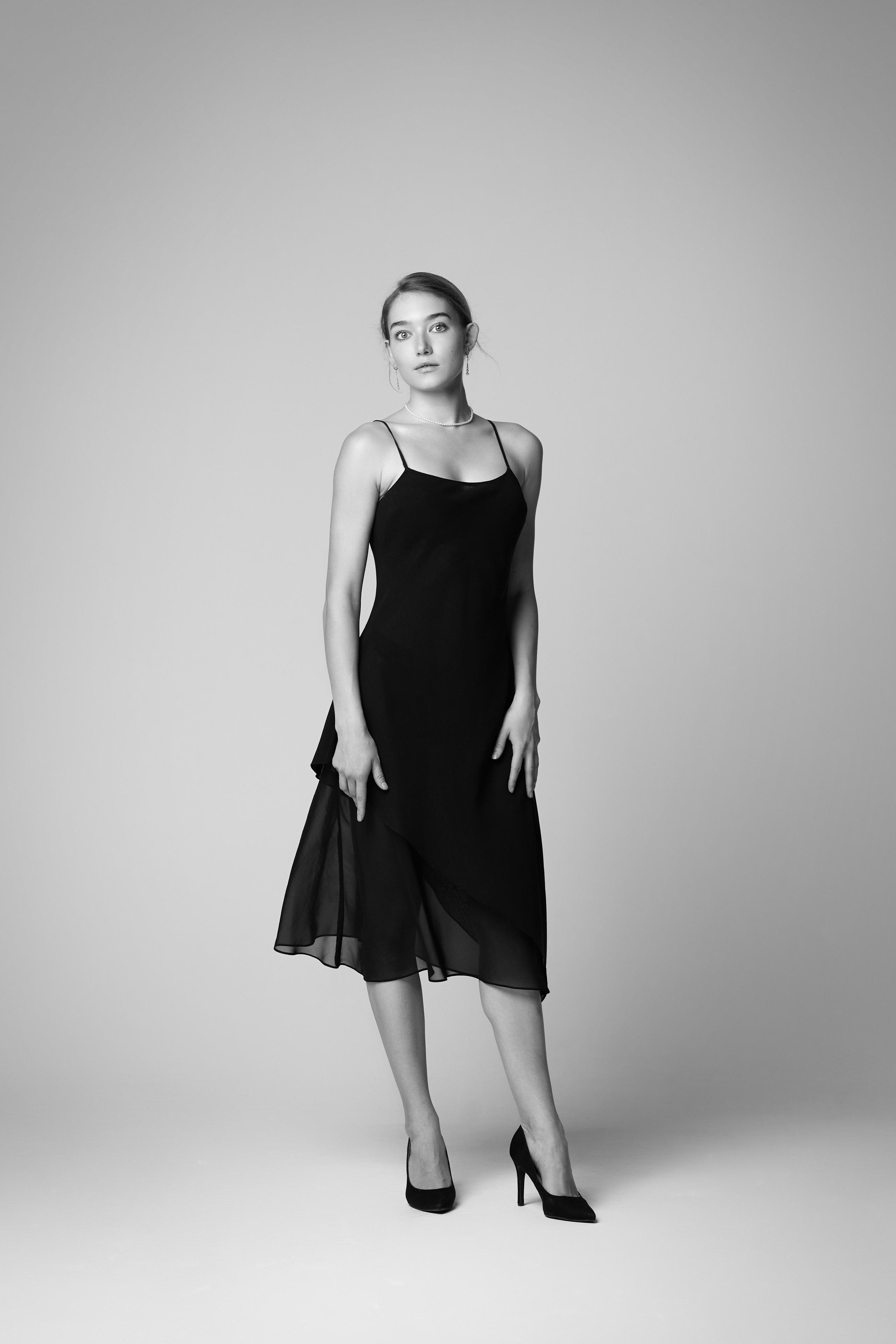 Алиса, светловолосая модель, одетая в свою белую рубашку, позирует на светлом фоне студии.