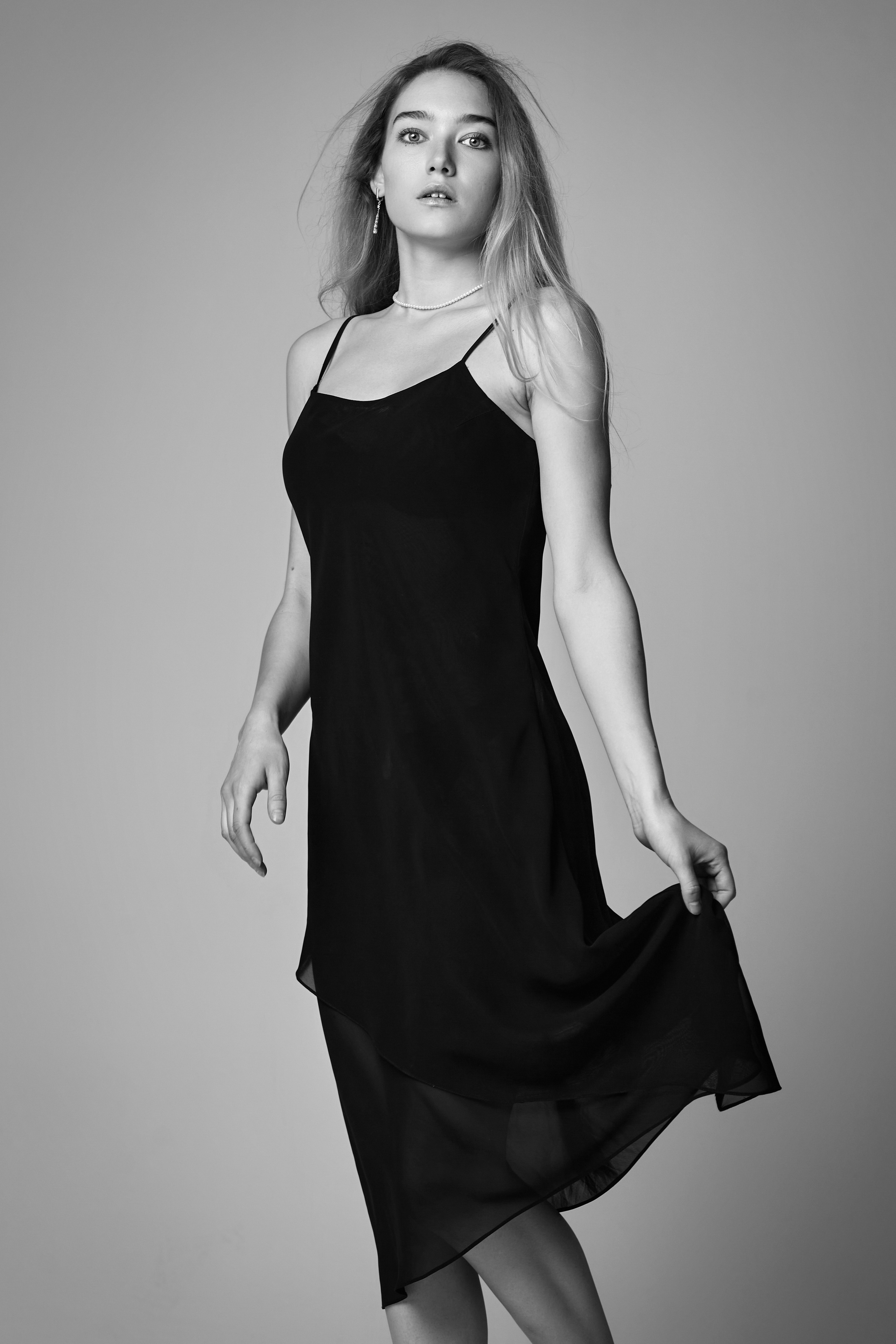 Алиса, светловолосая модель в платье, уверенно позирует на светлом фоне студии.