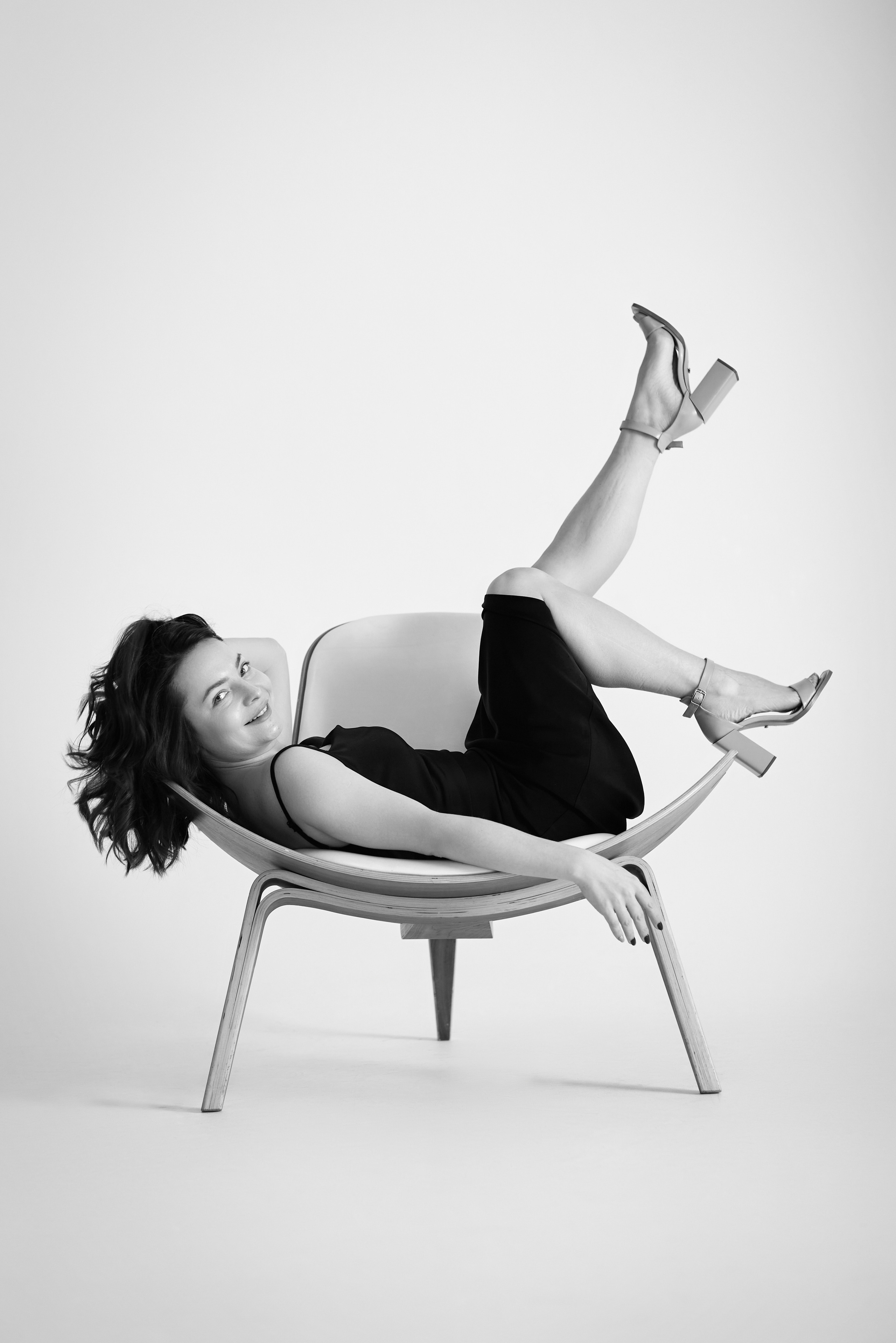 Темноволосая модель Татьяна стоит в светлом топике на фоне светлой стены в студии.