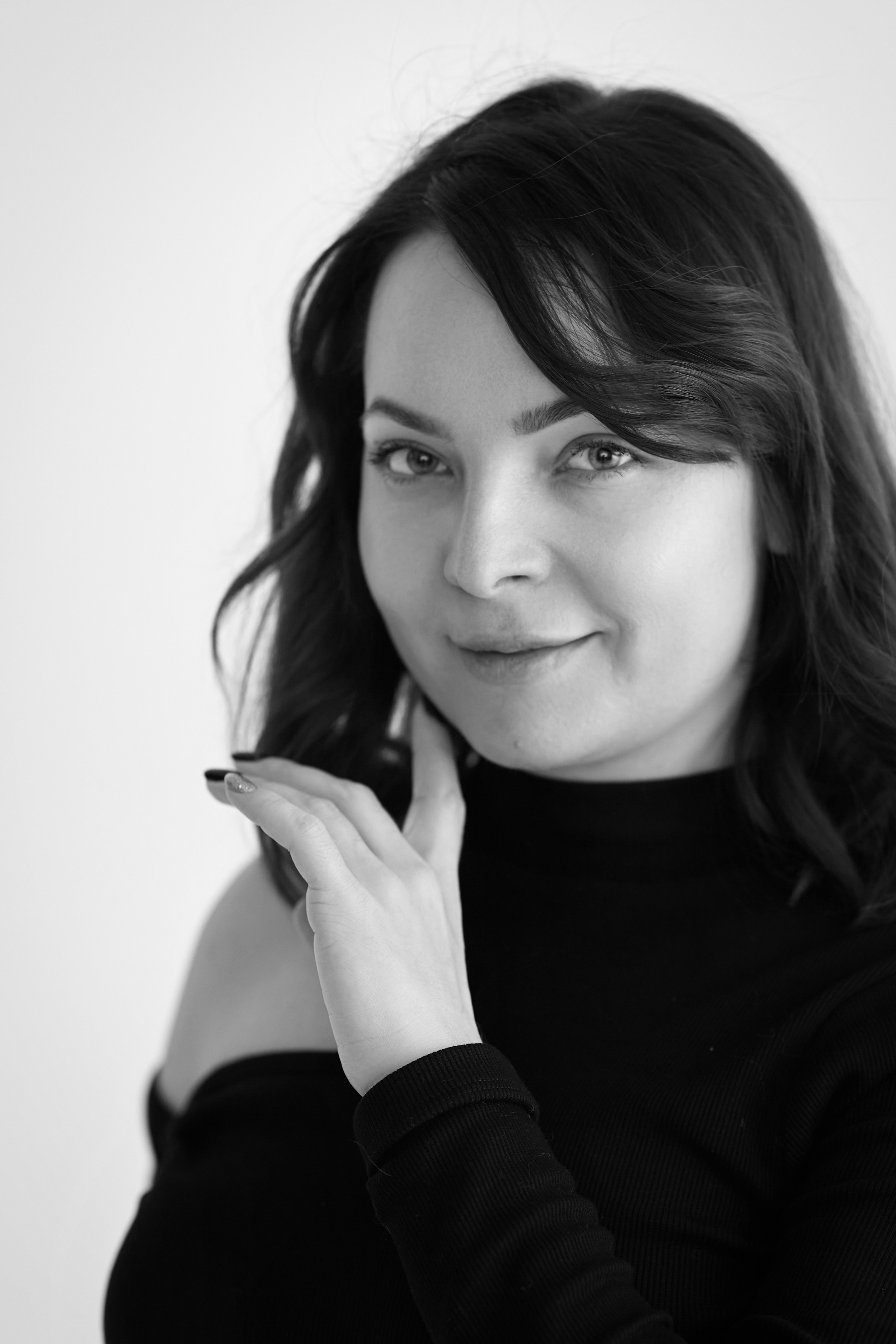 Темноволосая модель Татьяна на светлом фоне в светлом платье, рубашке или топике, позирующая на стуле с непринужденной улыбкой.