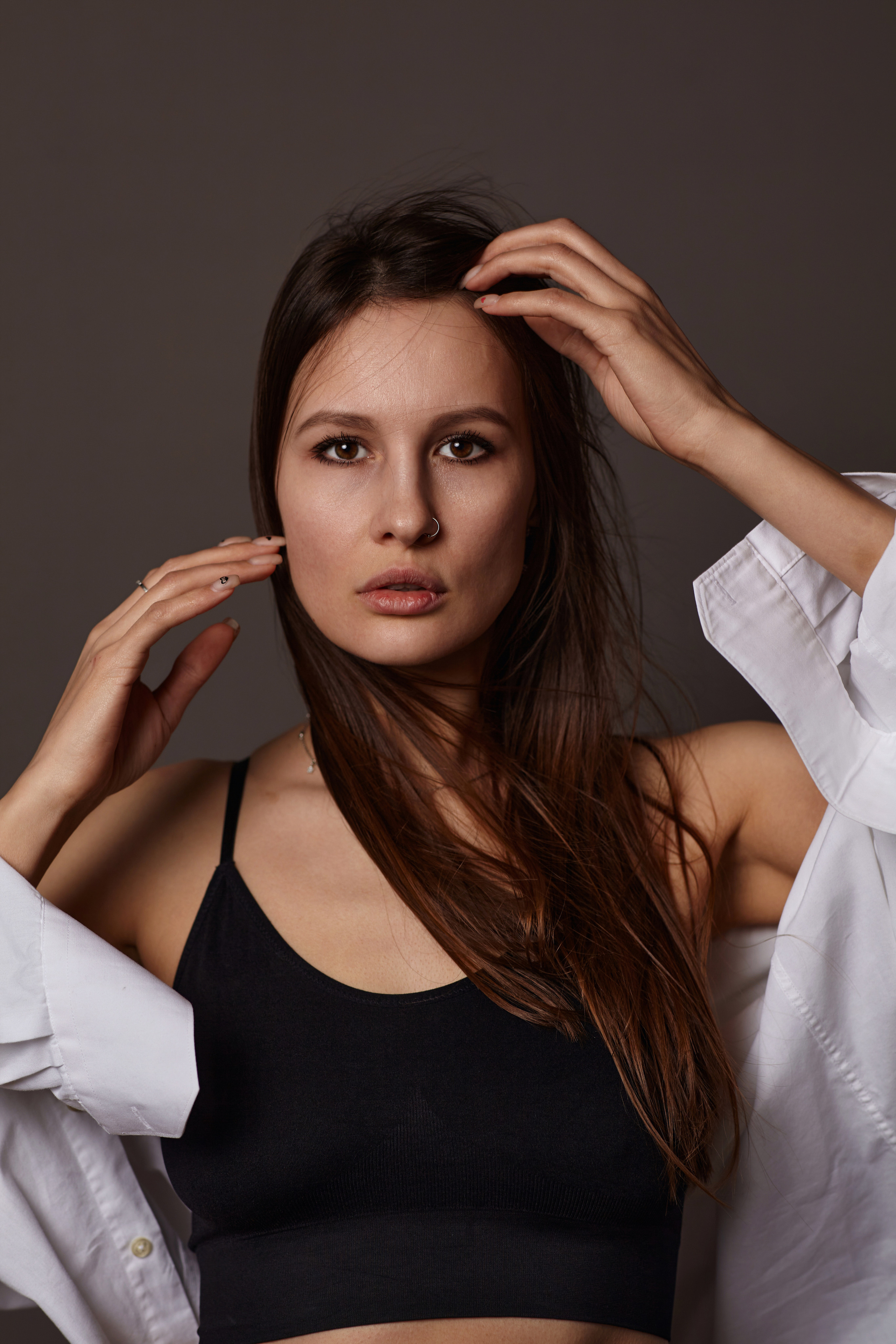 Красивая девушка с темными волосами стоит на темном фоне в фотостудии.