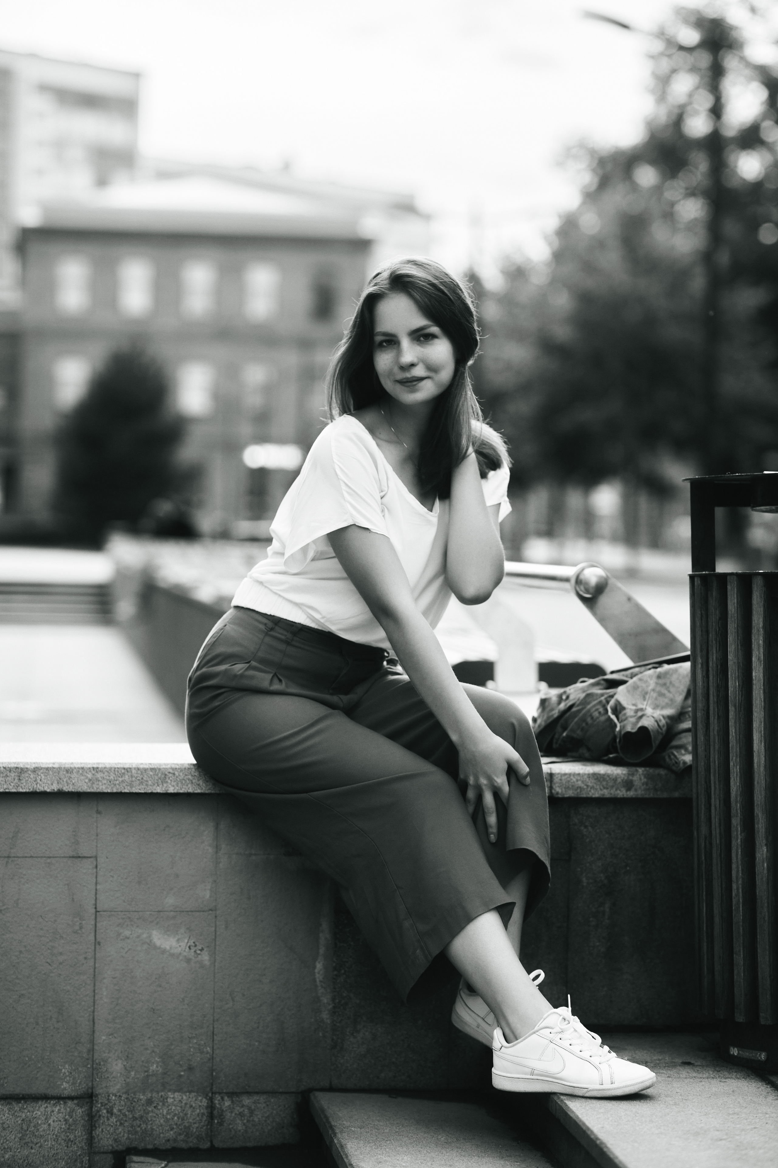 Дарья, одетая в светлую кофту и широкие брюки, позирует на улице Москвы.