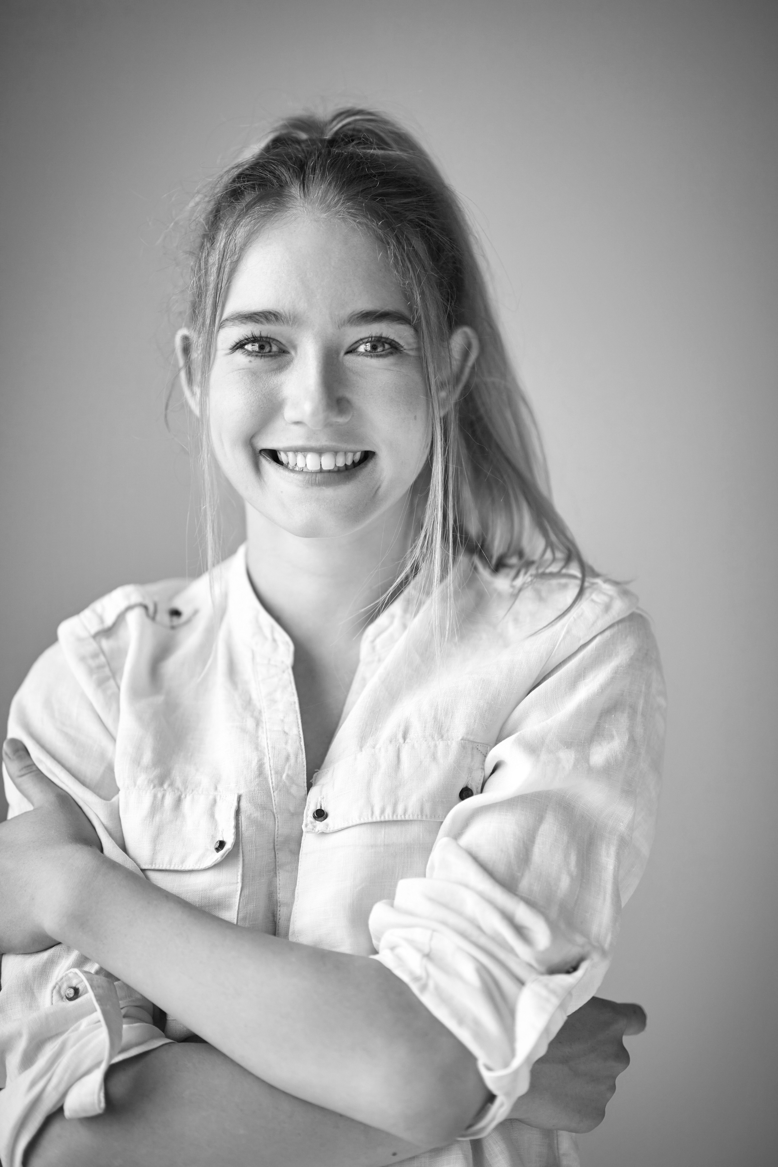 Алиса, очаровательная модель, воплощает образ в студии на светлом фоне, представив себя в платье или рубашке.