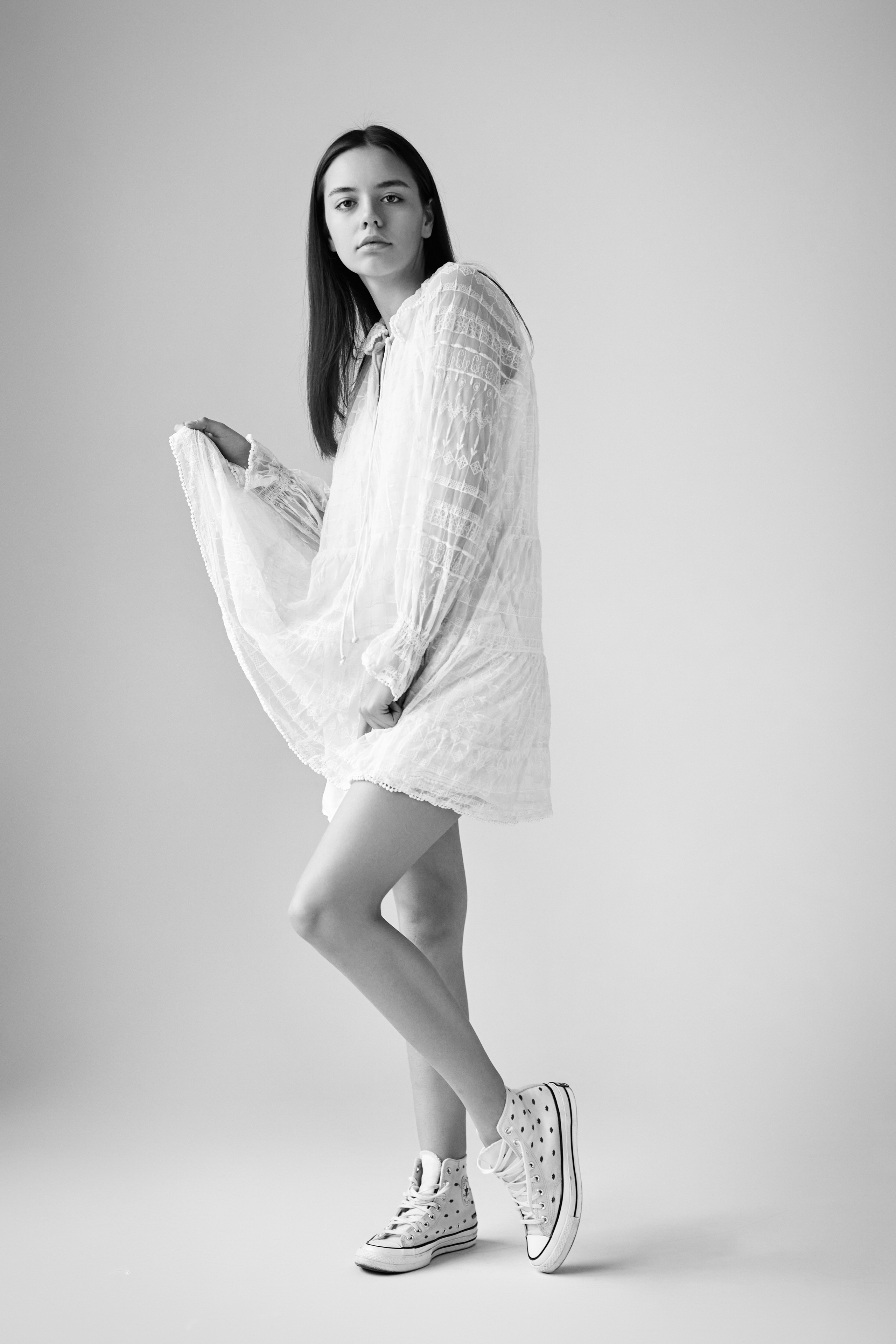 Темноволосая модель Амина в студии на светлом фоне одета в рубашку, ее волосы разделены на прямую челку.