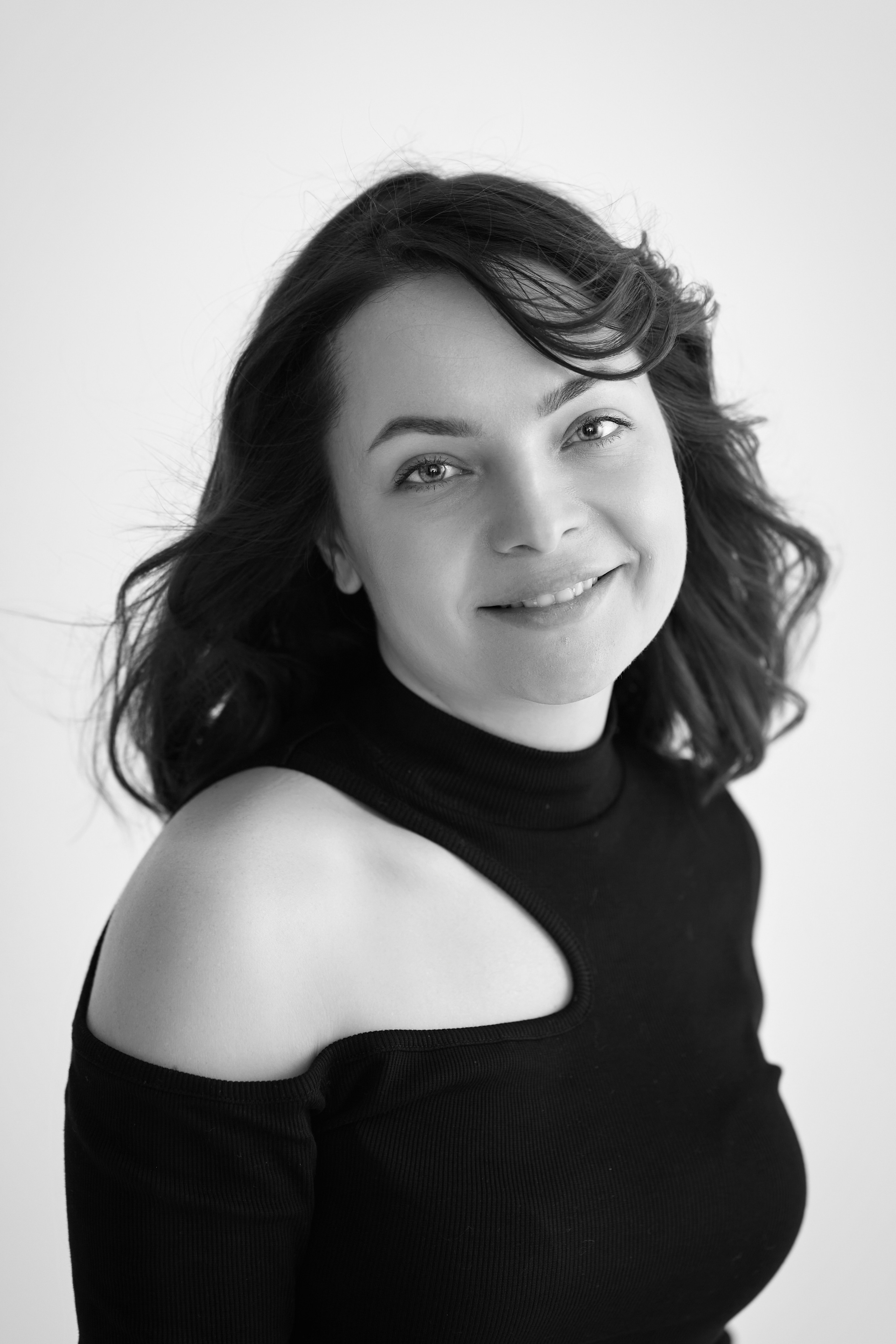 Темноволосая модель Татьяна находится на фоне светлой стены в светлом платье на студии.