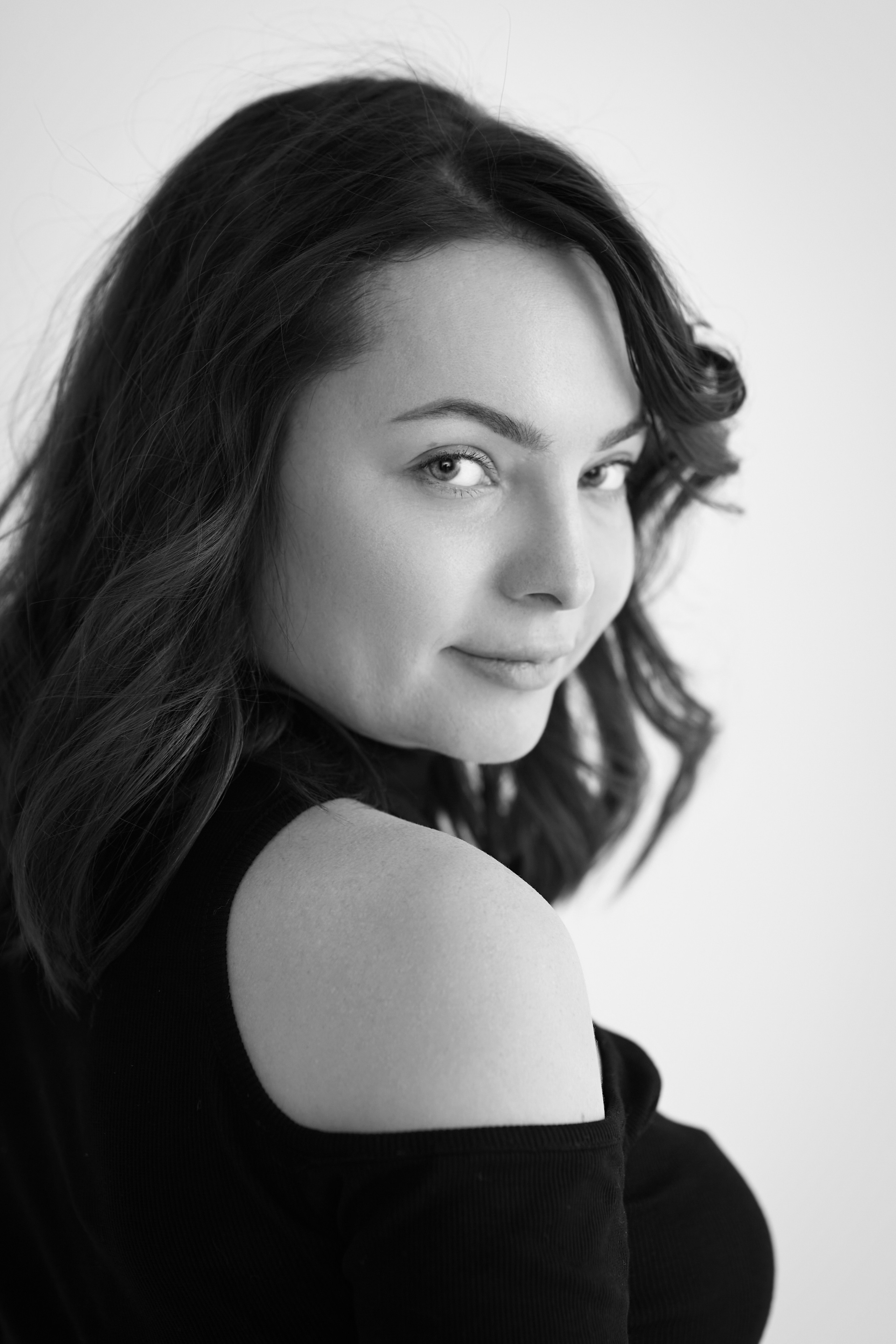 Темноволосая модель Татьяна позирует на стуле в светлой рубашке на фоне светлого фона.