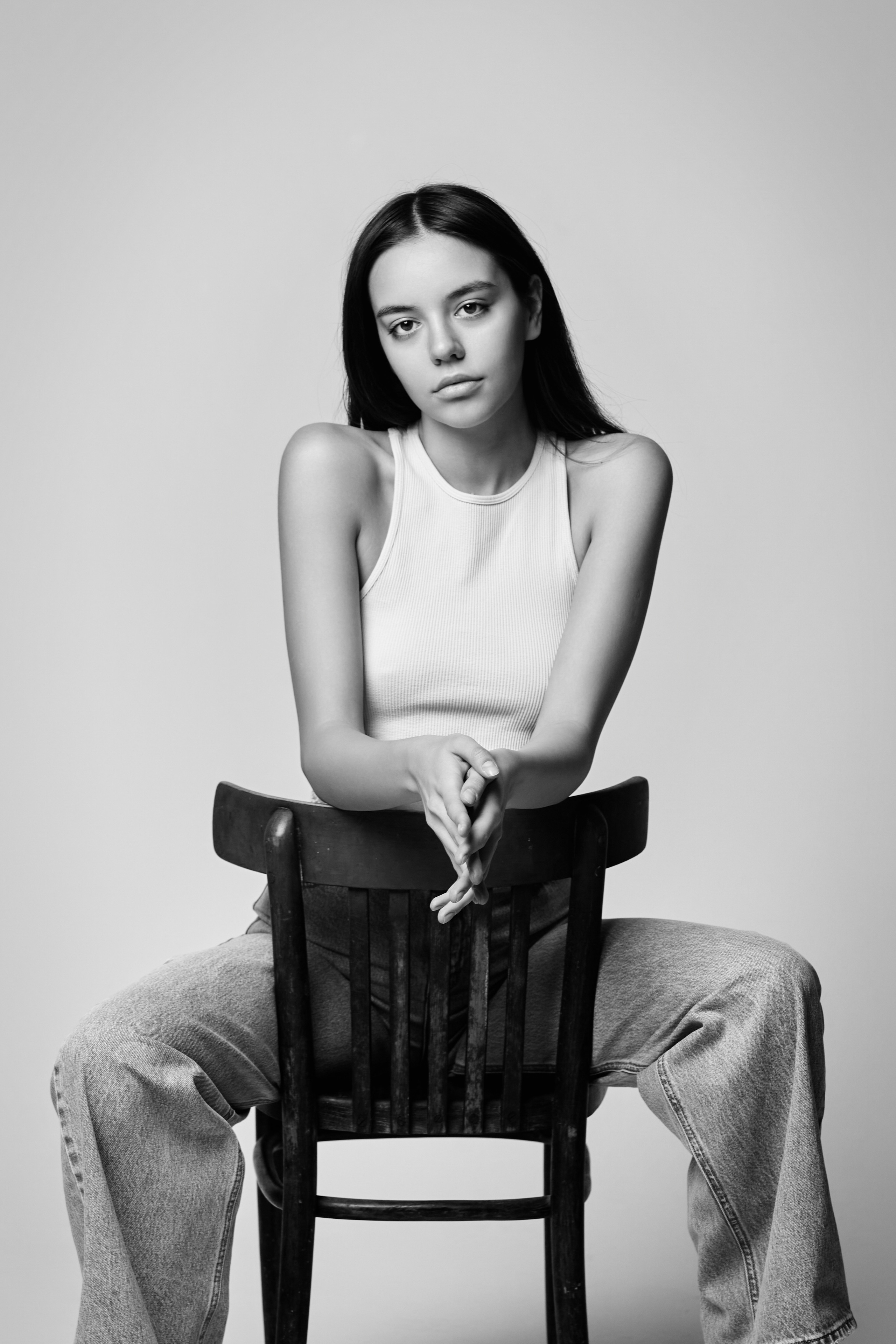 Темноволосая модель Амина на светлом фоне в светлом платье с разрезом на ноге.