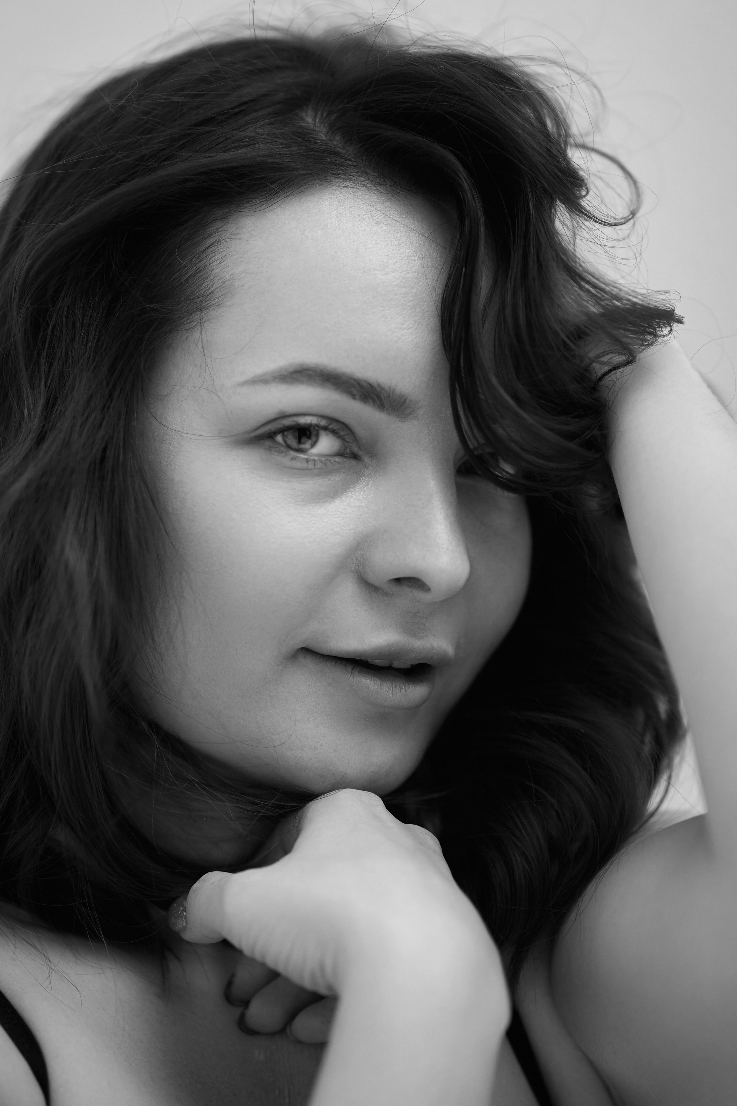 Темноволосая модель Татьяна в топике стоит на светлом фоне в студии.