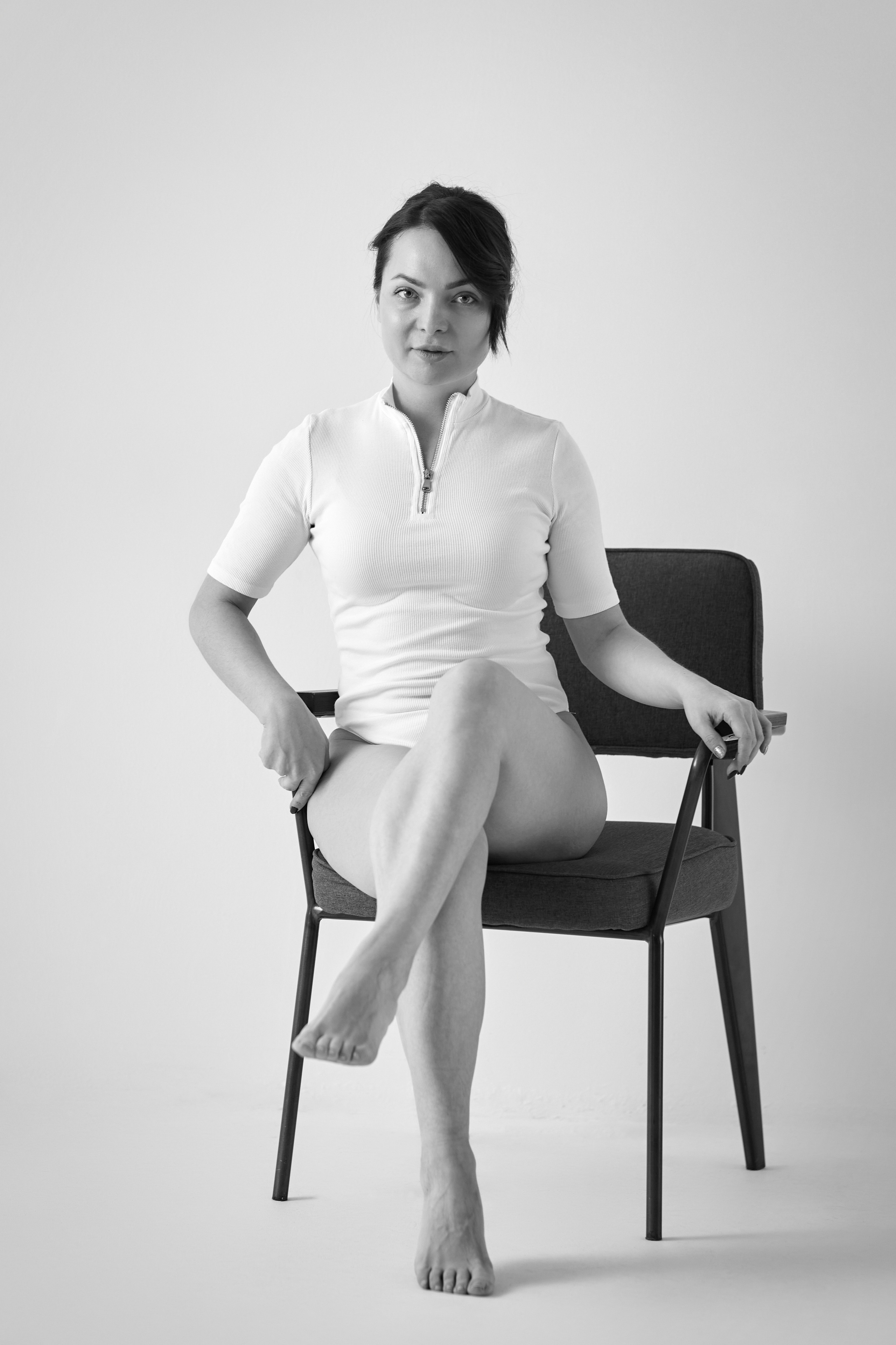 Темноволосая модель Татьяна стоит на фоне светлого фона в светлом топике в студии.