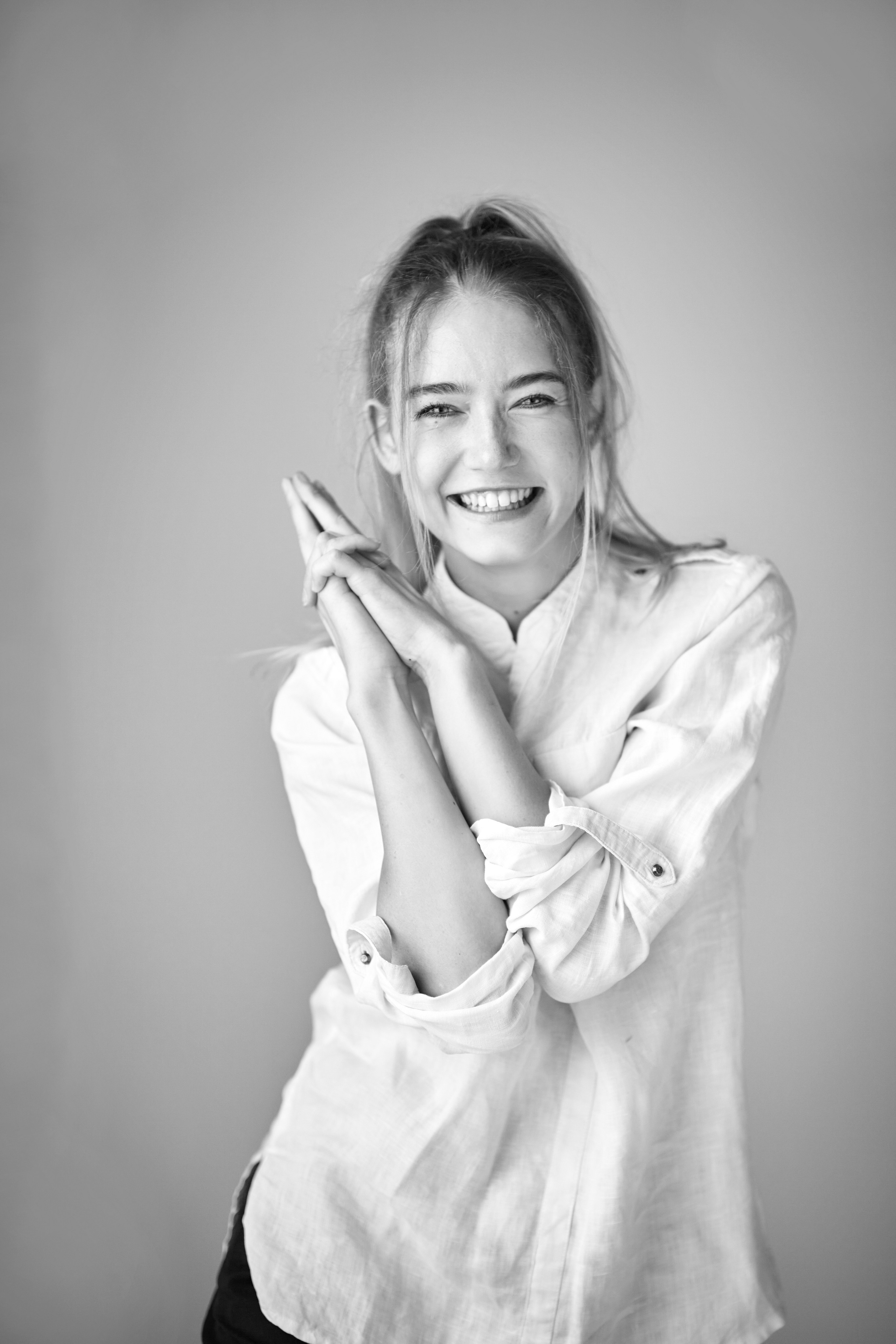 Светловолосая красавица Алиса в рубашке позирует на светлом фоне фотостудии.