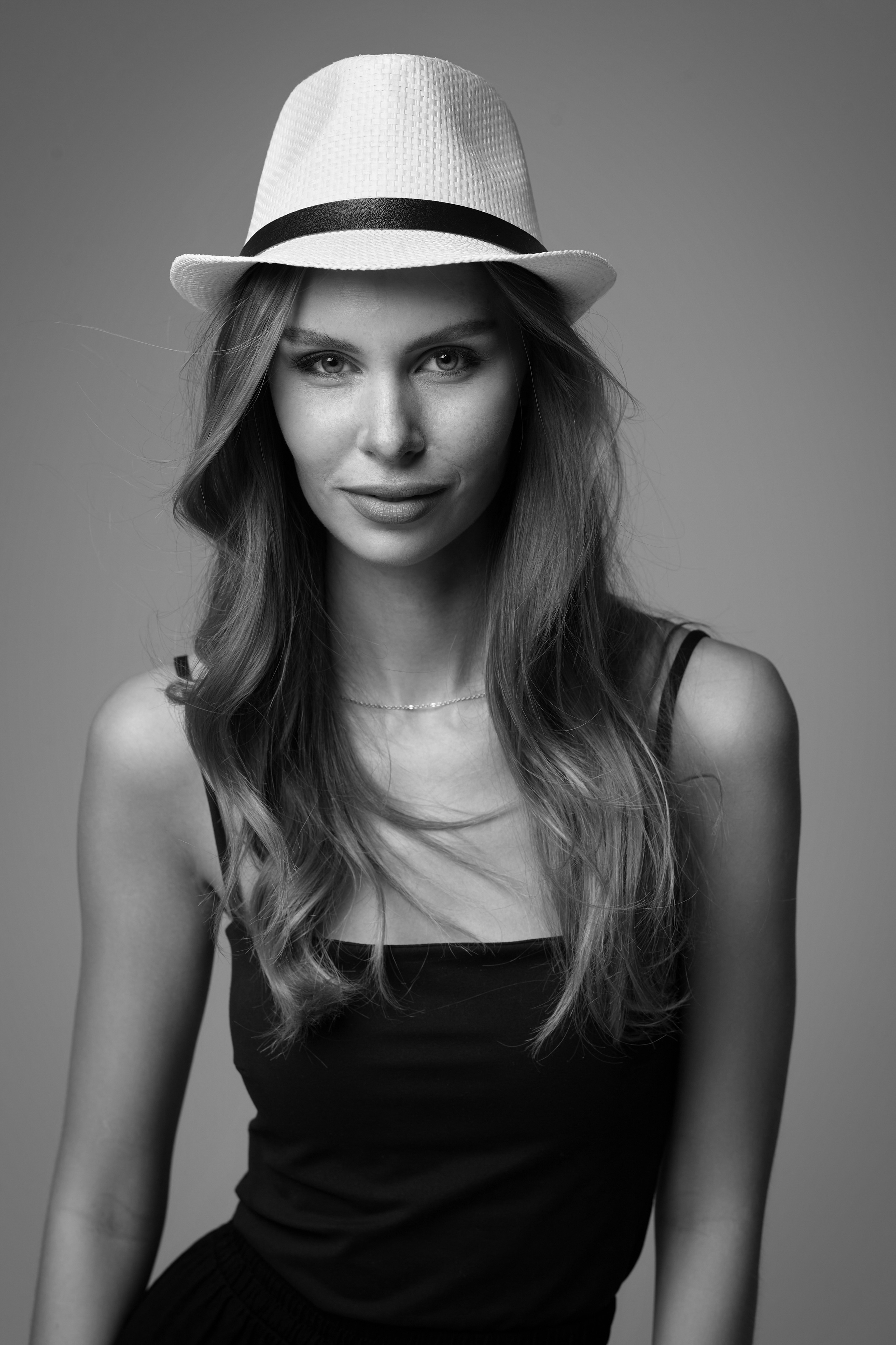 Элегантная темноволосая девушка в шляпе и очках на светлом фоне создаёт загадочный образ.