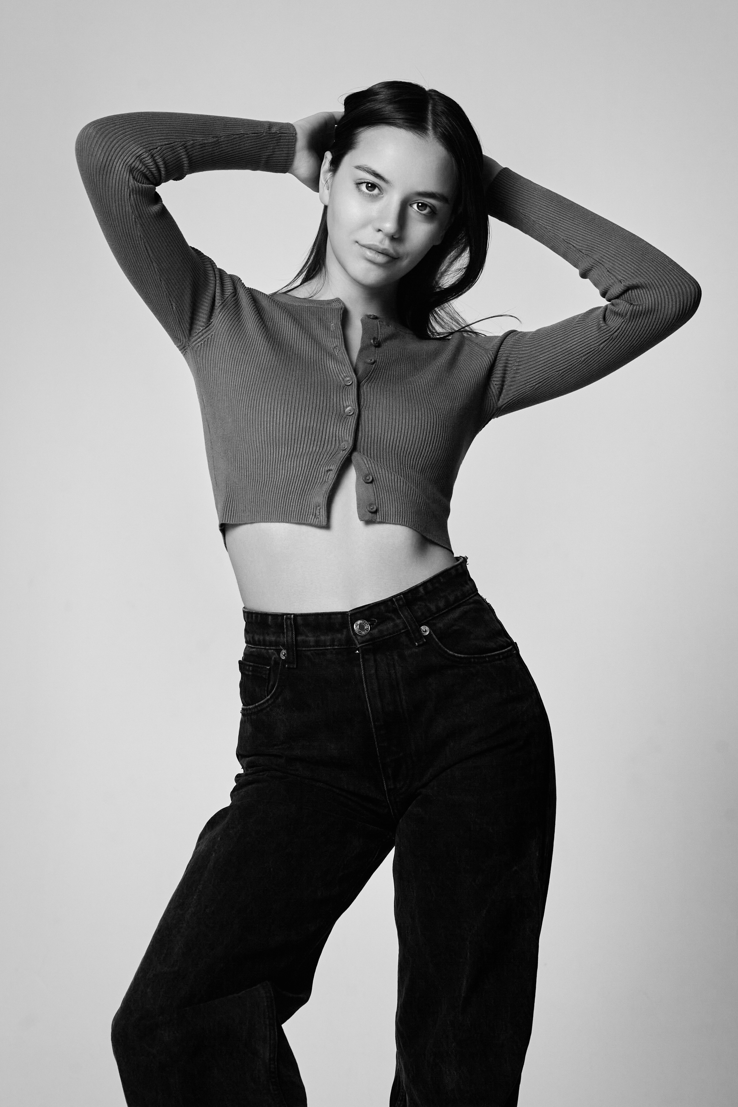 Темноволосая модель Амина на светлом фоне в белом платье-футляре с высоким вырезом.