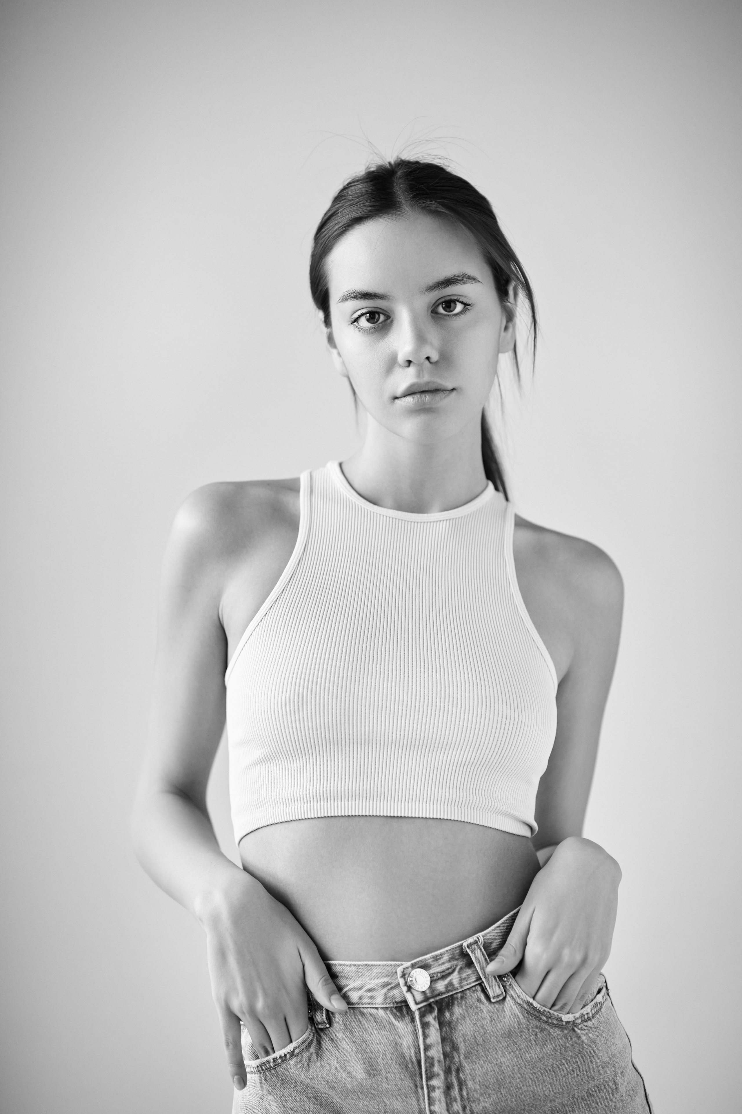 Красивая темноволосая Амина в светлом платье, рубашке или топике на фоне студии.