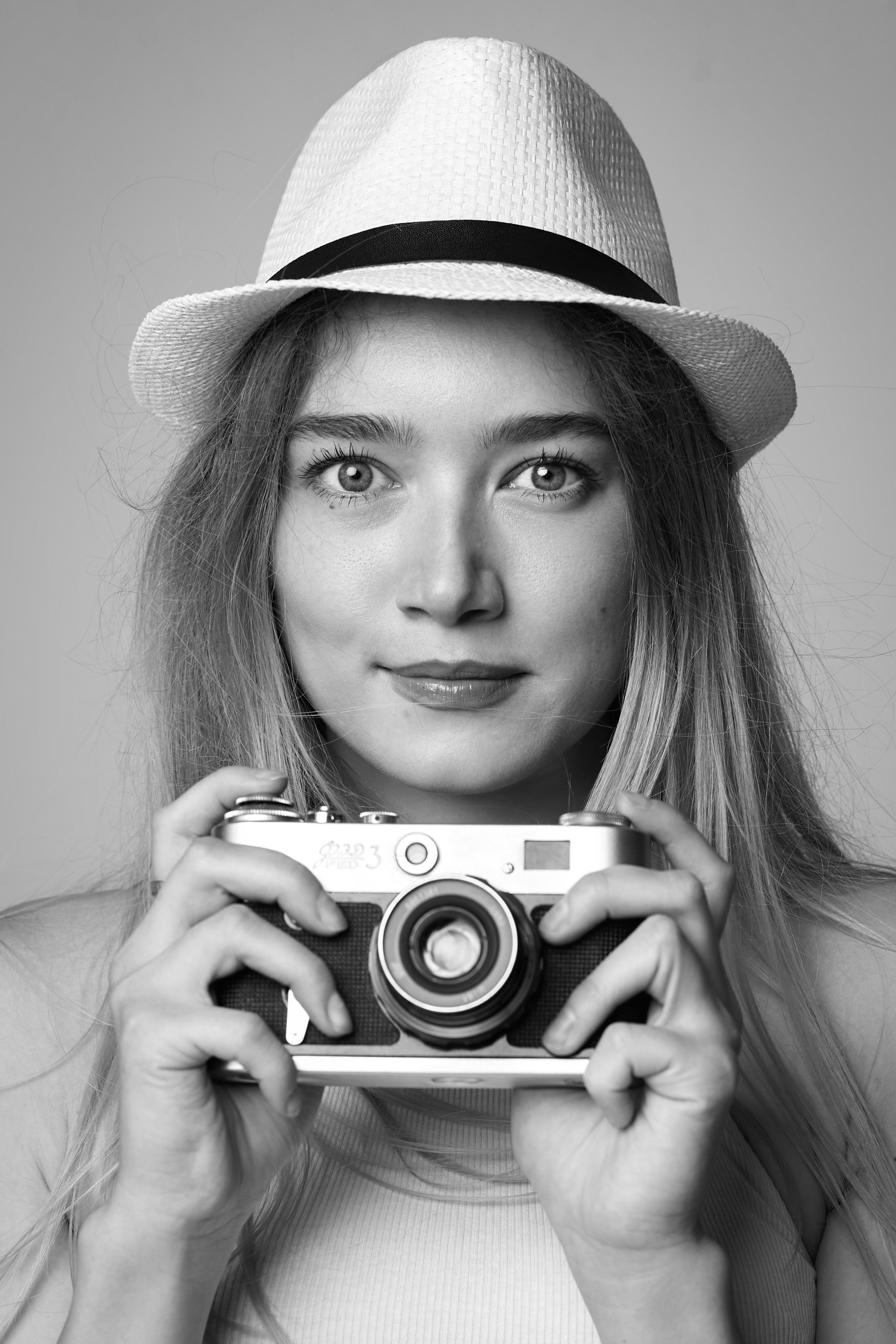 Светловолосая модель Алиса в студии на светлом фоне в красном платье-футляре и черных туфлях.