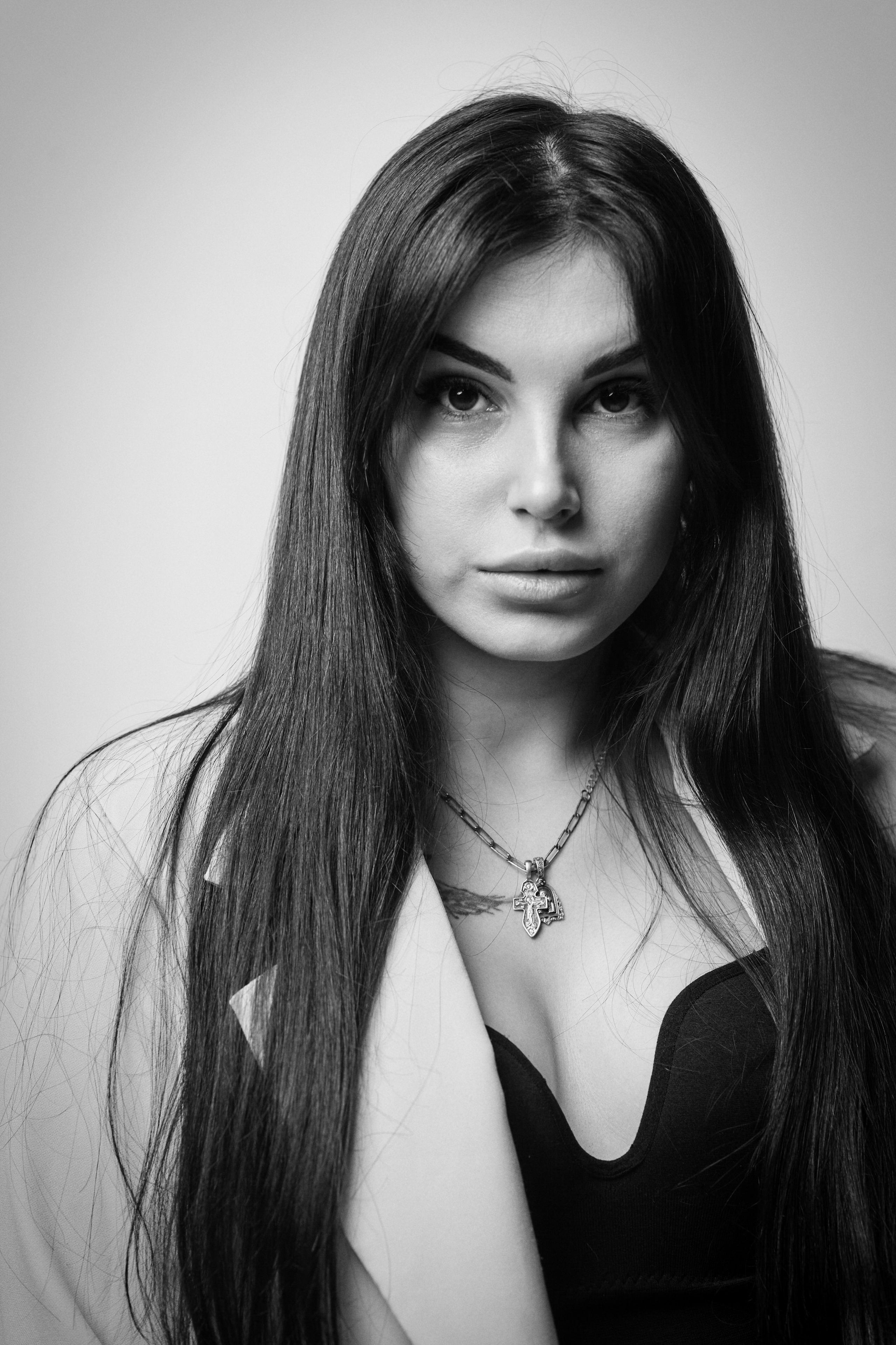 Темноволосая модель Карина в костюме на светлом фоне студии, строгий и сдержанный образ