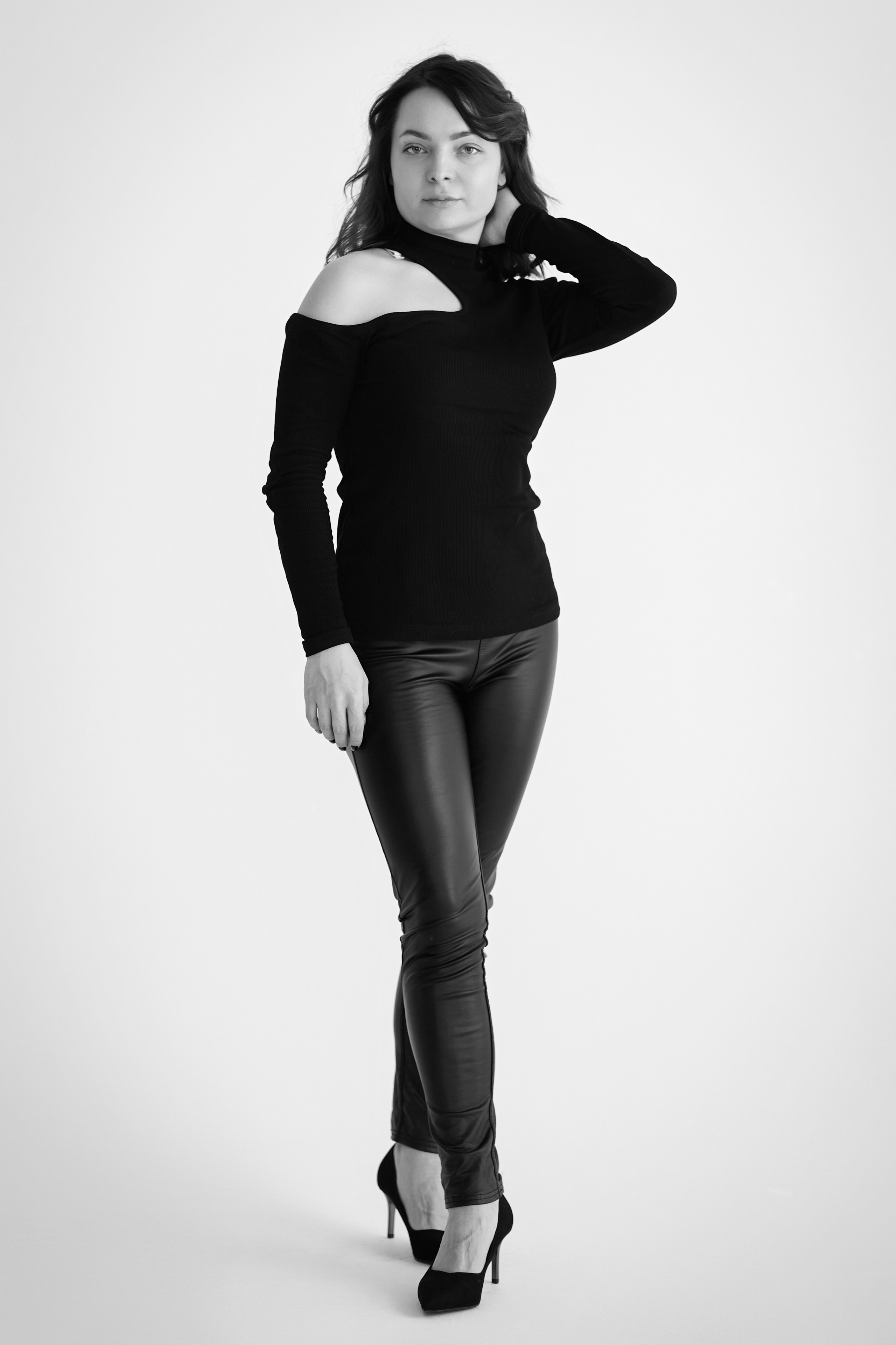 Темноволосая Татьяна в светлом платье стоит на светлом фоне в студии.