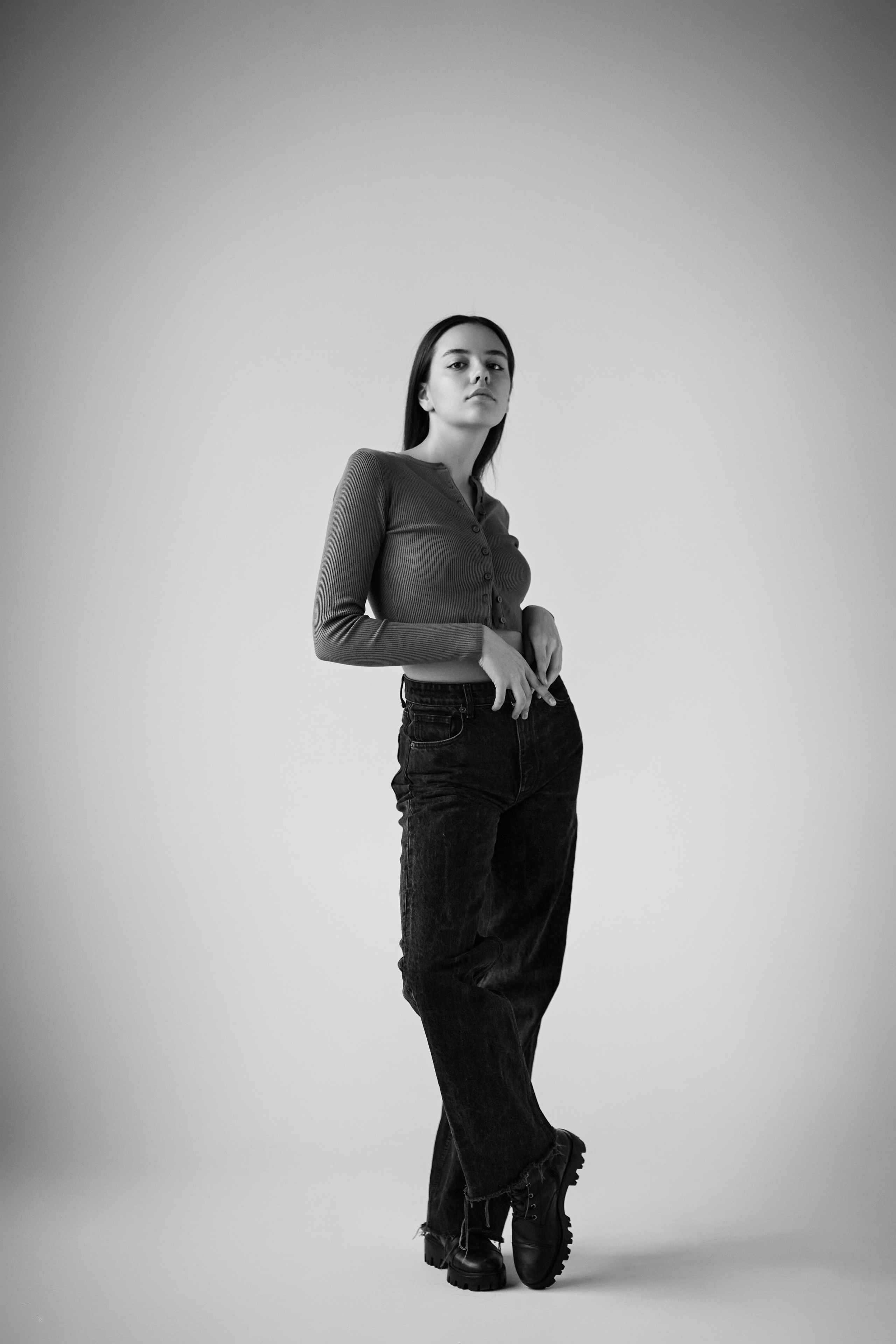 Темноволосая модель Амина на светлом фоне в светлой рубашке и длинной юбке с разрезом.