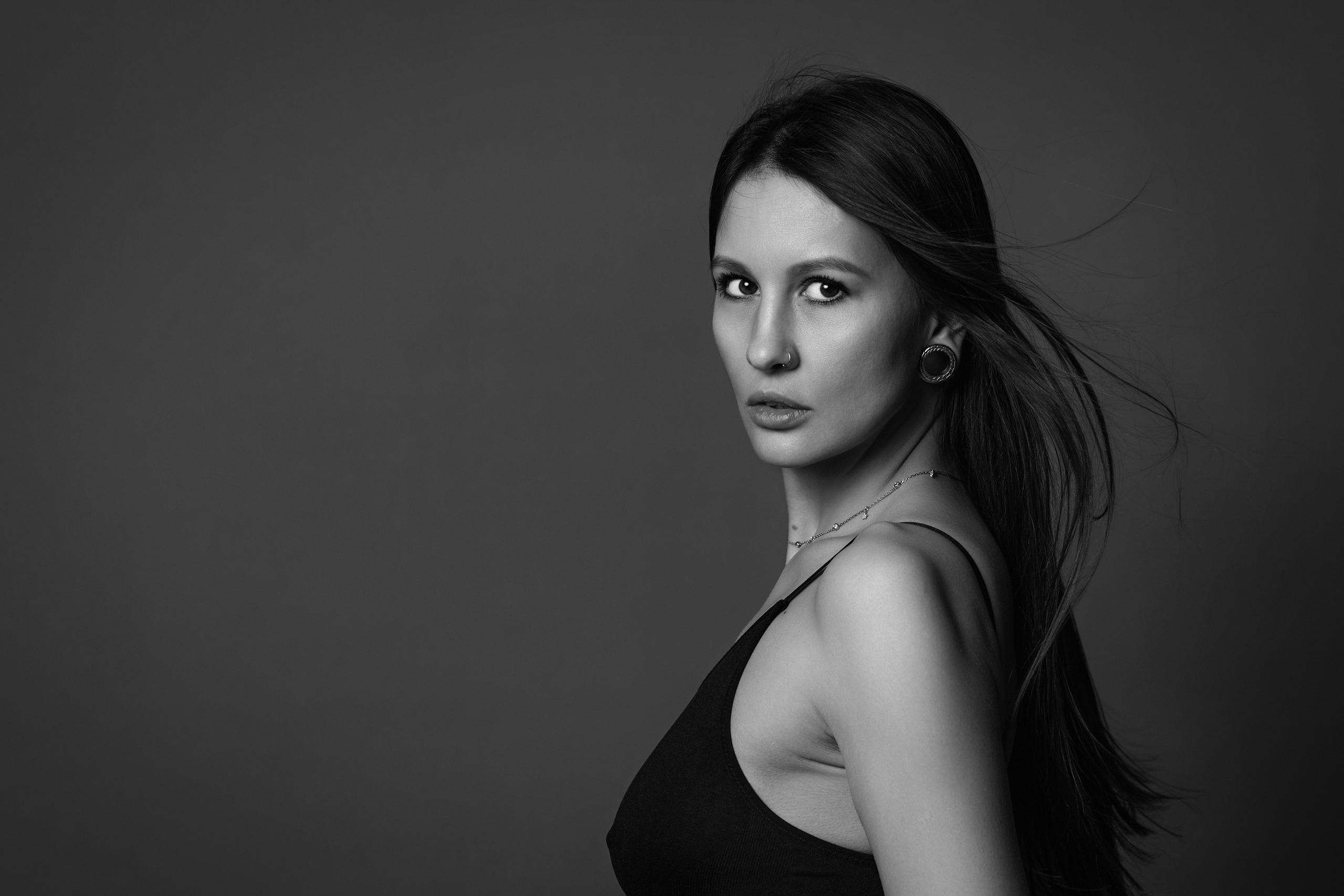 Молодая темноволосая женщина стоит на циклораме с светлым фоном, глядя прямо в камеру.