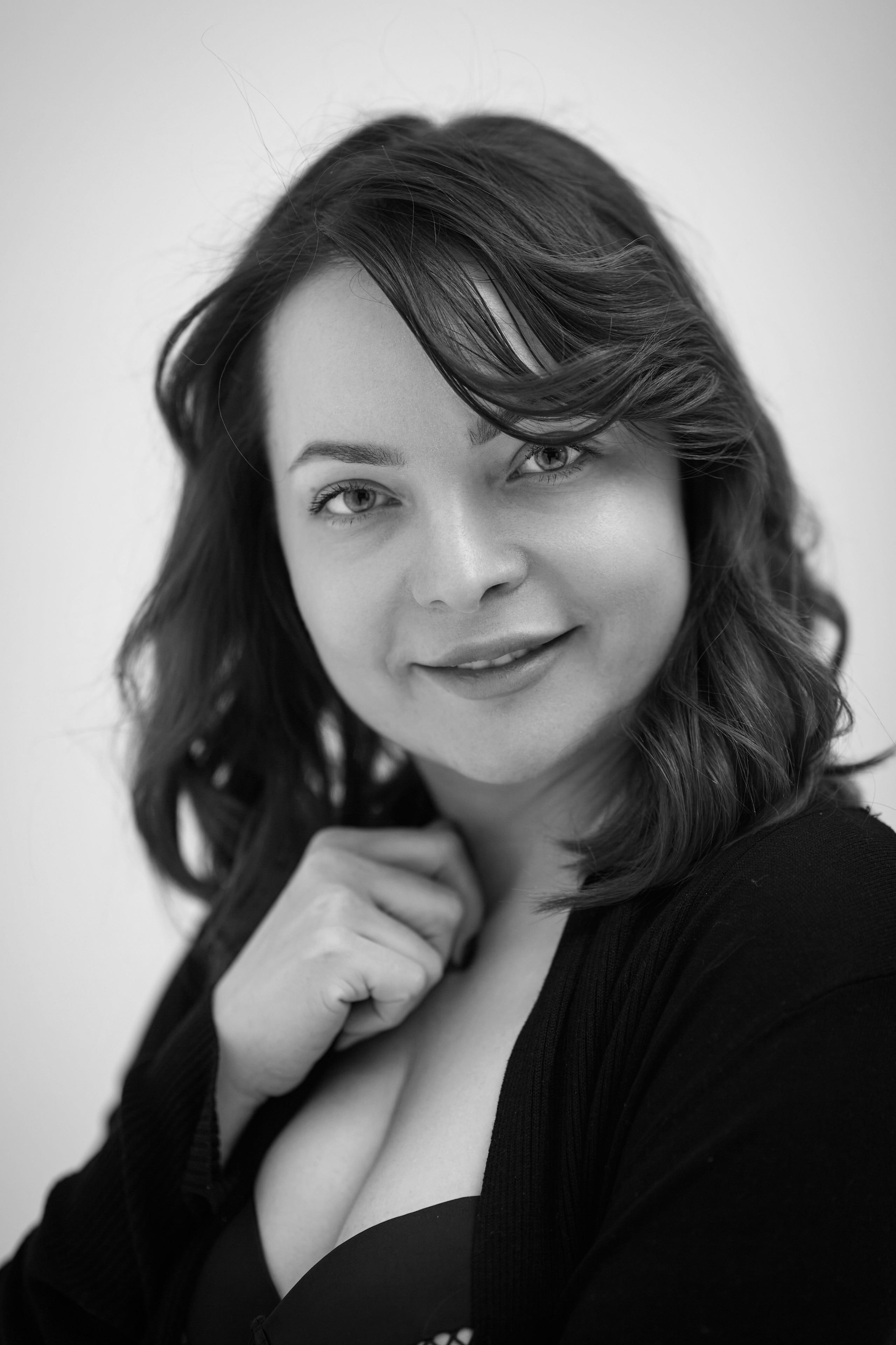 Темноволосая модель Татьяна стоит на стуле в светлом топике на фоне светлого фона в студии.