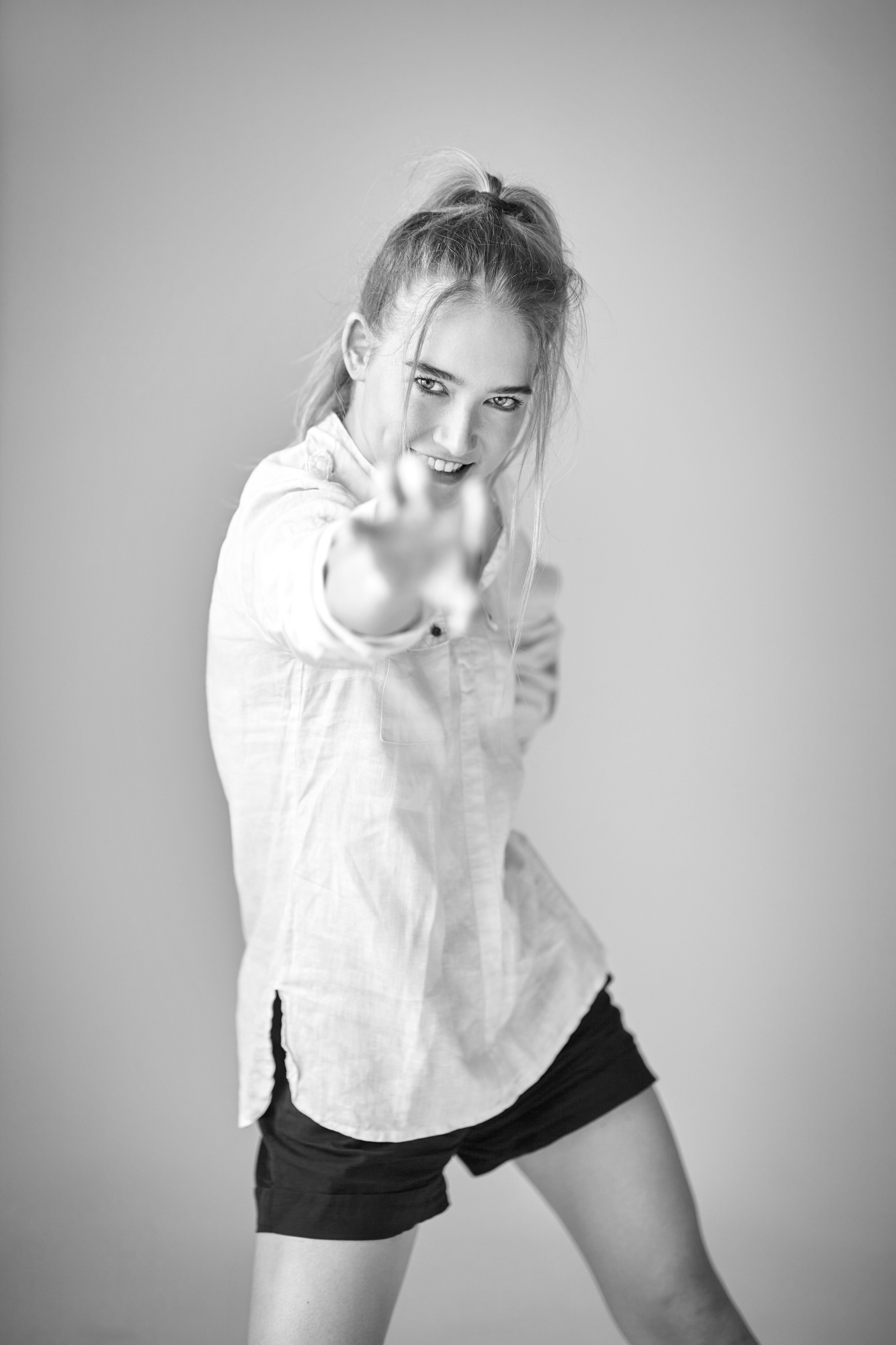 В студии на светлом фоне, светловолосая модель Алиса выглядит потрясающе в своей белоснежной рубашке.