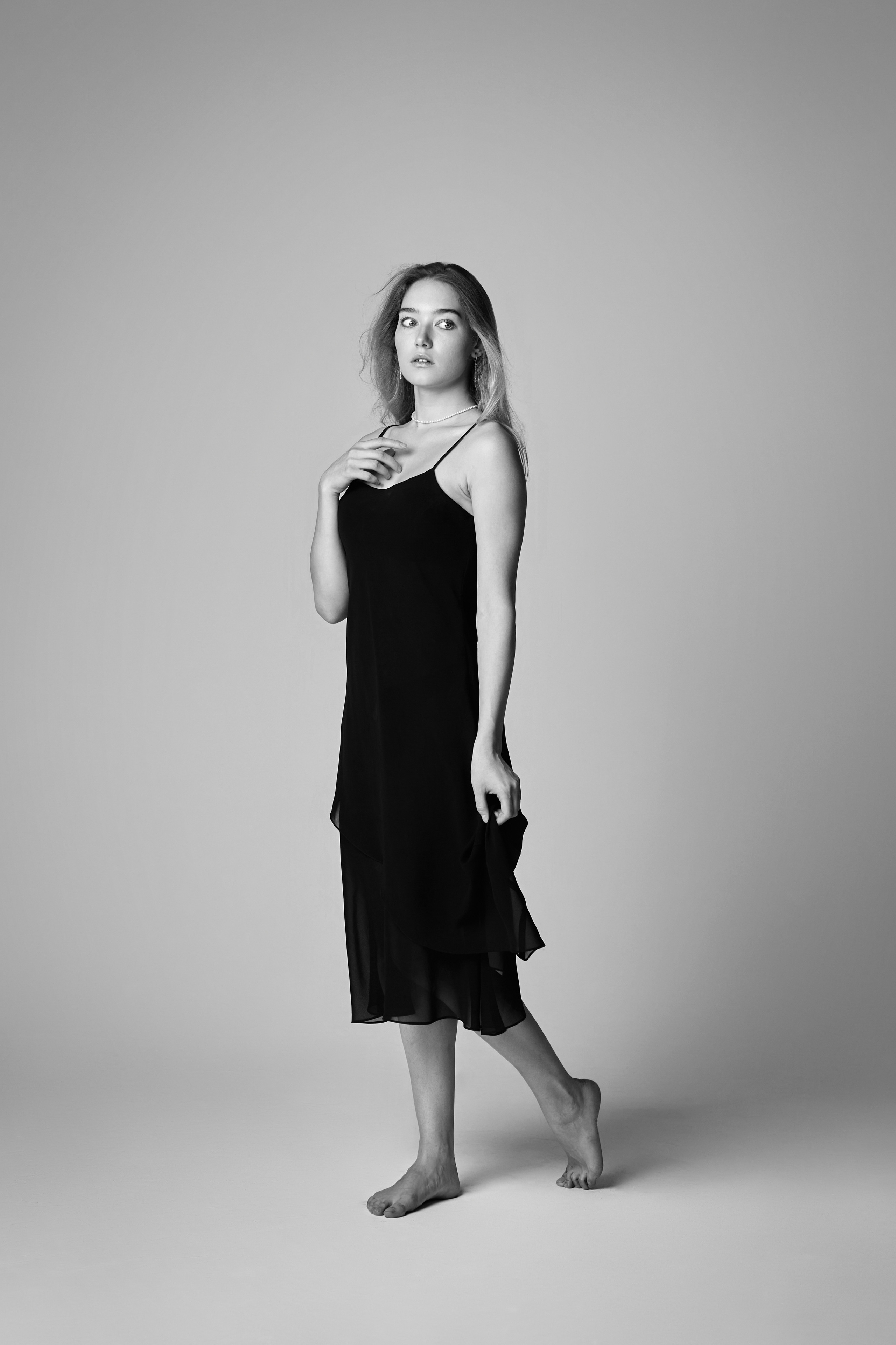 Алиса, красивая модель с светлыми волосами, одетая в своё великолепное платье, фотографируется на светлом фоне студии.