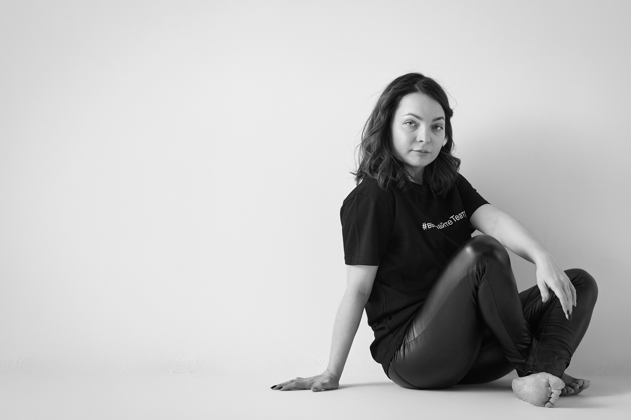 Темноволосая модель Татьяна на светлом фоне, в светлом платье, рубашке или топике или на стуле, смотрящая на камеру с непринужденной улыбкой.