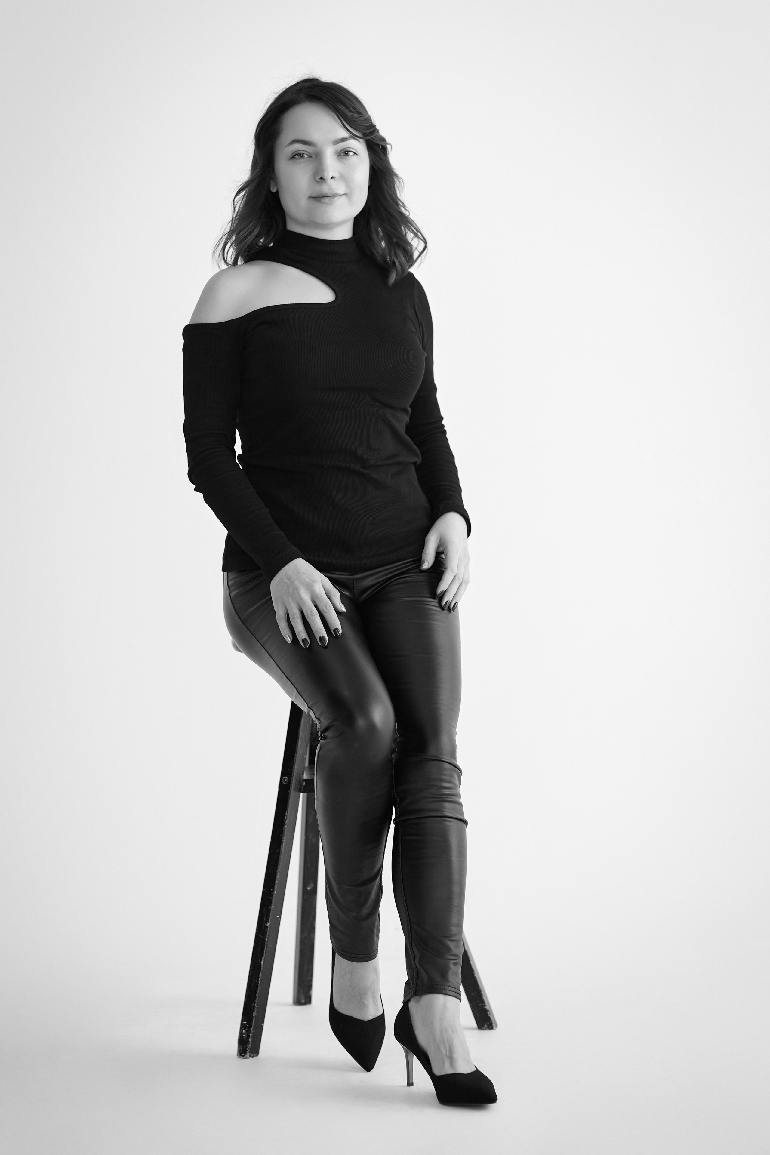 Темноволосая модель Татьяна стоит на светлом фоне в светлом топике на фоне светлой стены.