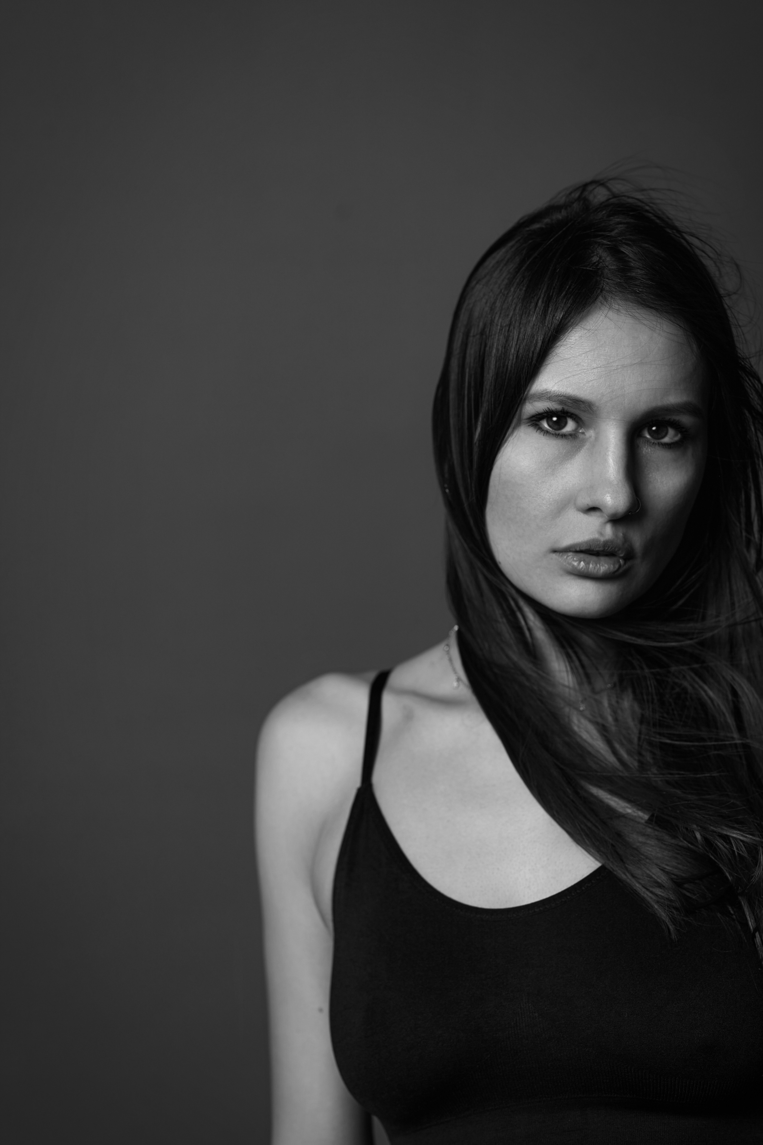 Темноволосая модель в студии на светлом фоне создаёт красивые позы.