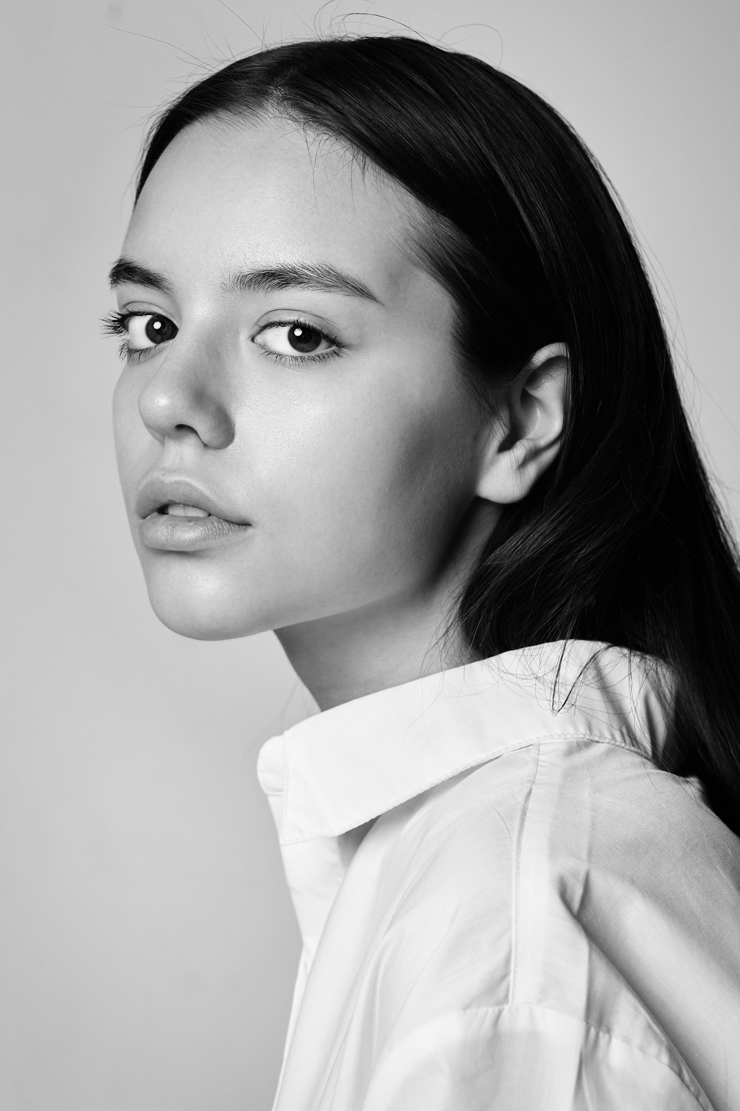 Темноволосая Амина в студии на светлом фоне одета в топик, ее глаза выглядят загадочно.