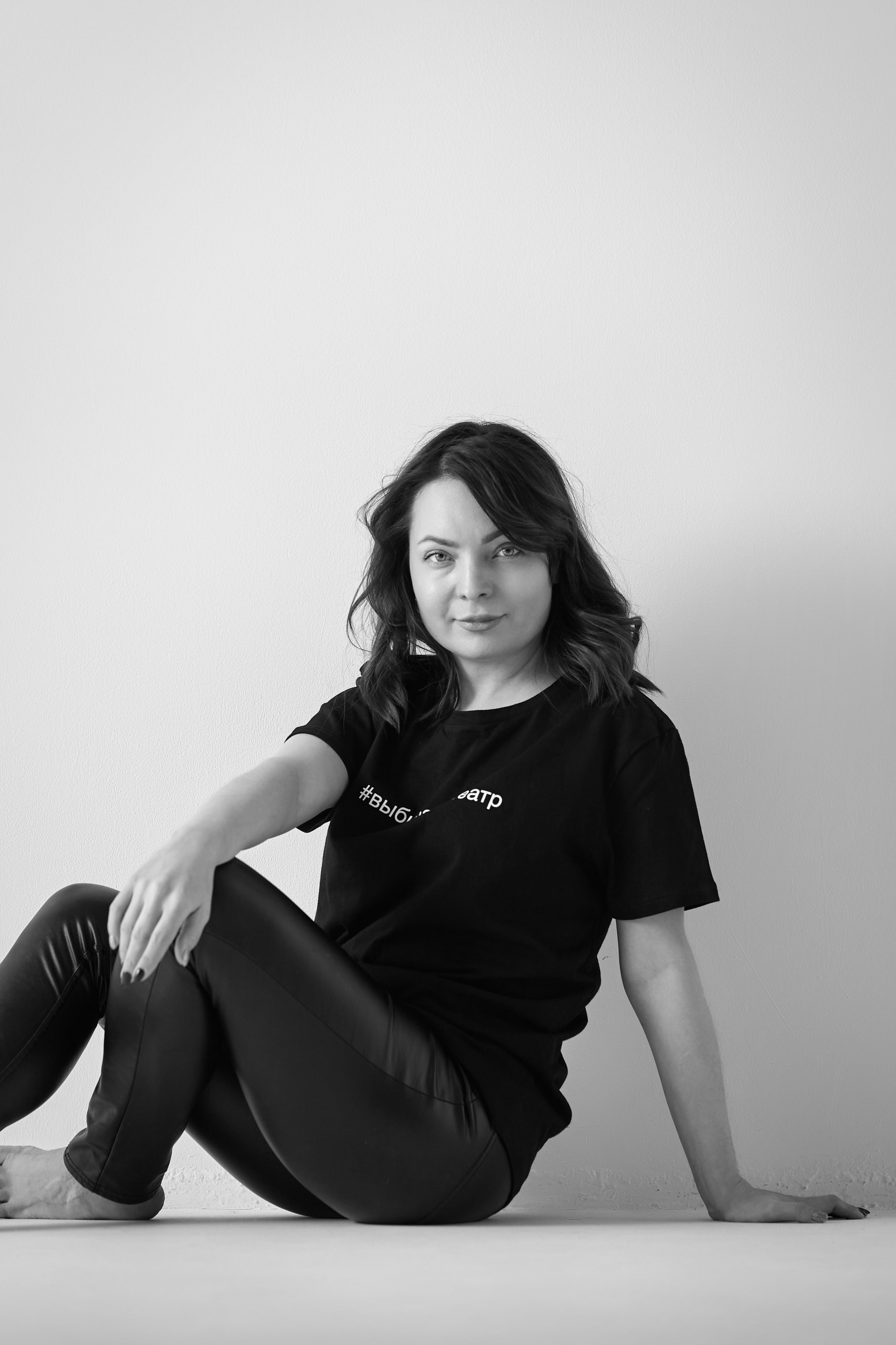 Темноволосая модель Татьяна стоит на фоне светлого фона в светлой рубашке на студии.