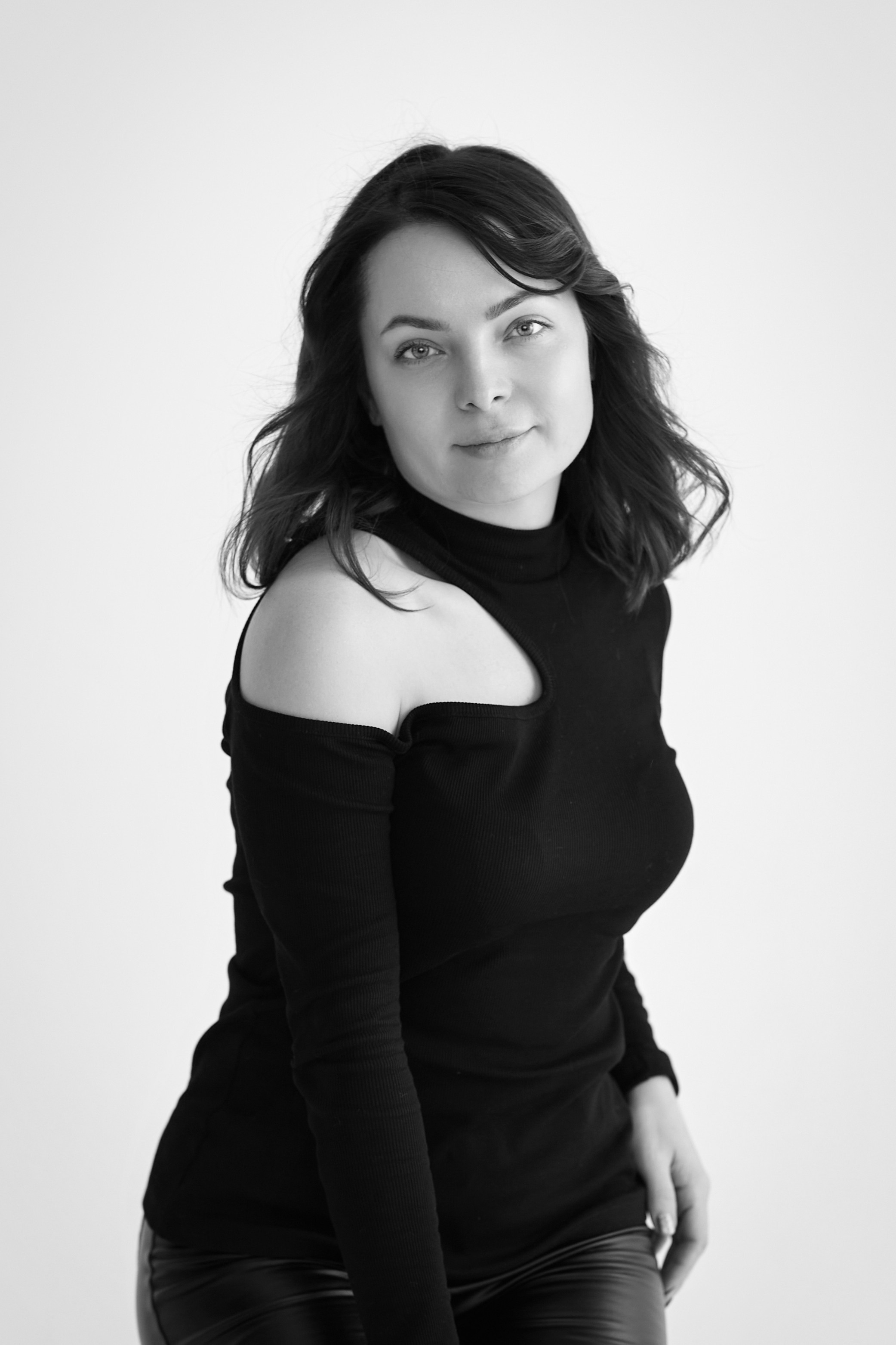 Студийный снимок темноволосой модели Татьяны на светлом фоне, в светлом платье, рубашке или топике, сидящей на стуле.