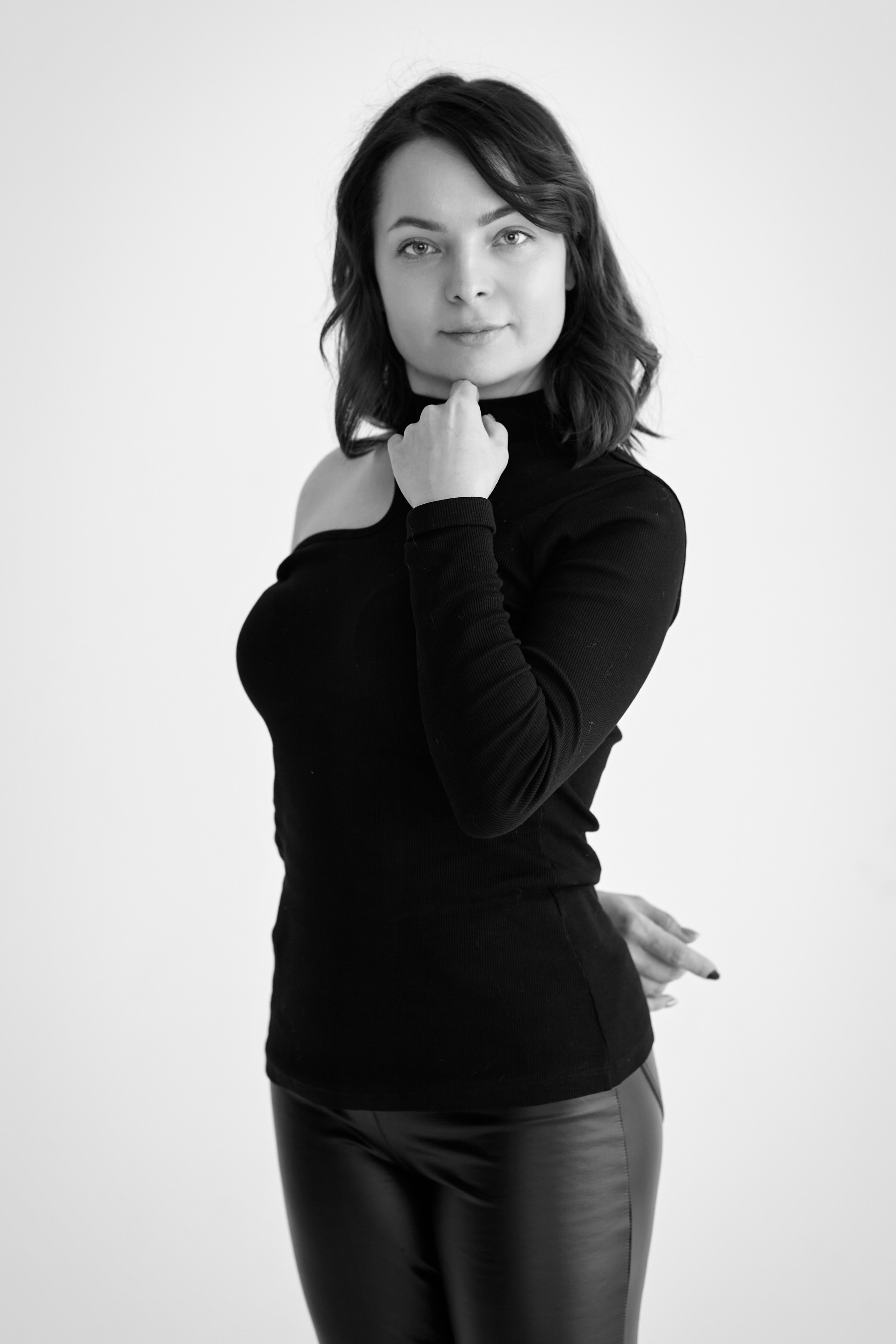 Темноволосая модель Татьяна сидит на стуле в светлом платье на фоне светлой стены.