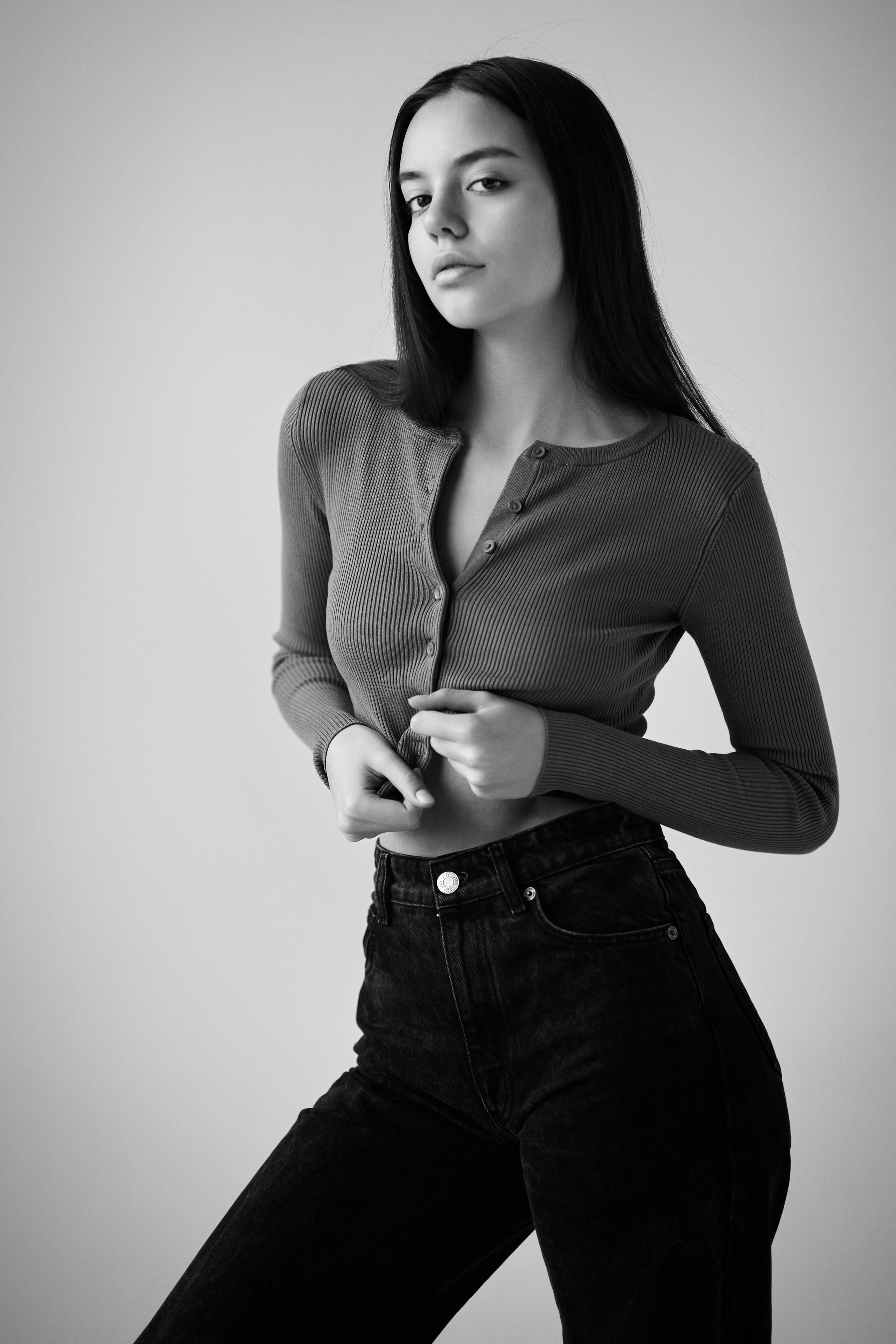 Модель Амина в рубашке стоит на светлом фоне в студии, ее волосы укладываются в небольшой хвостик.