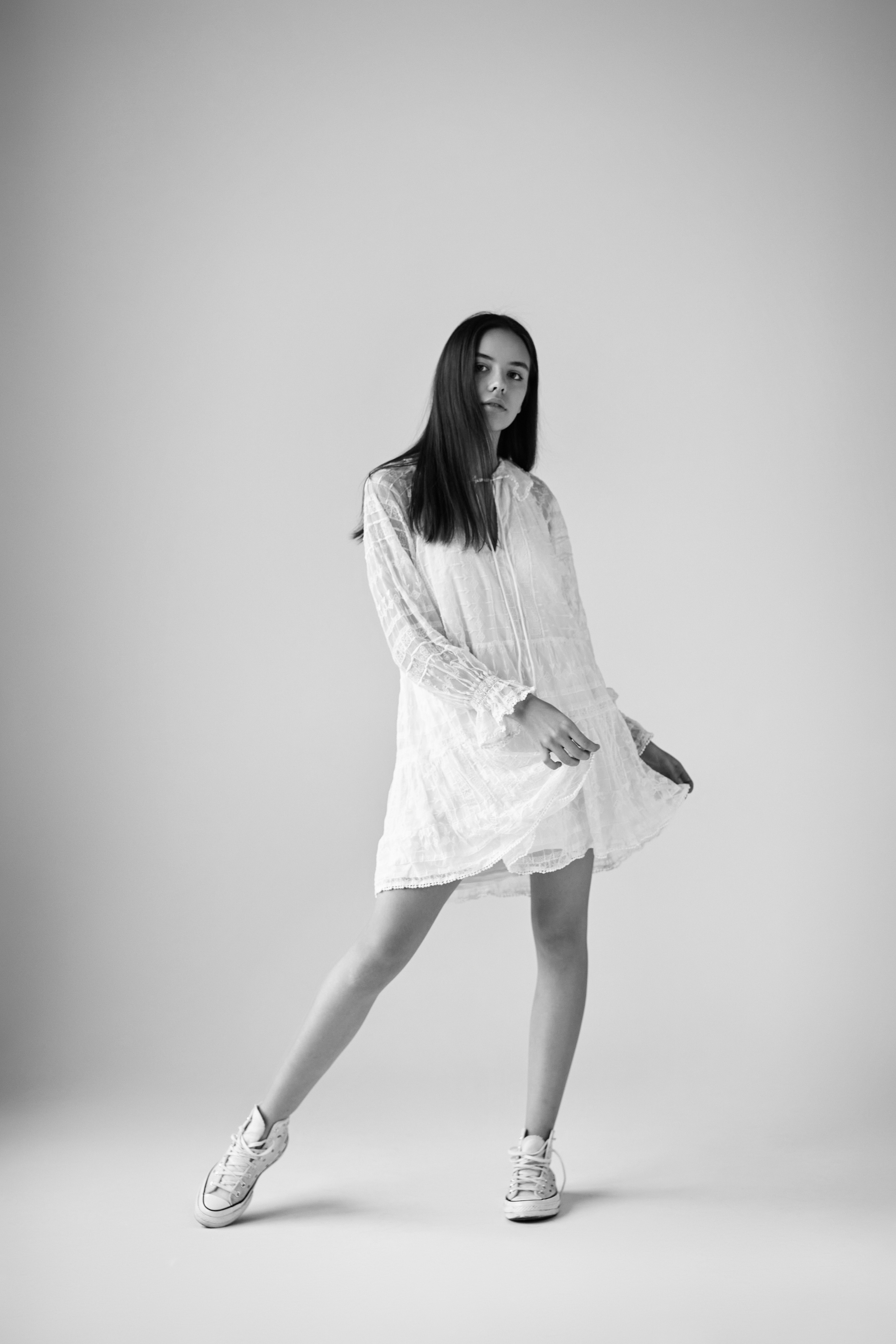 Темноволосая Амина в студии на светлом фоне одета в светлое платье, ее губы выглядят сочными.