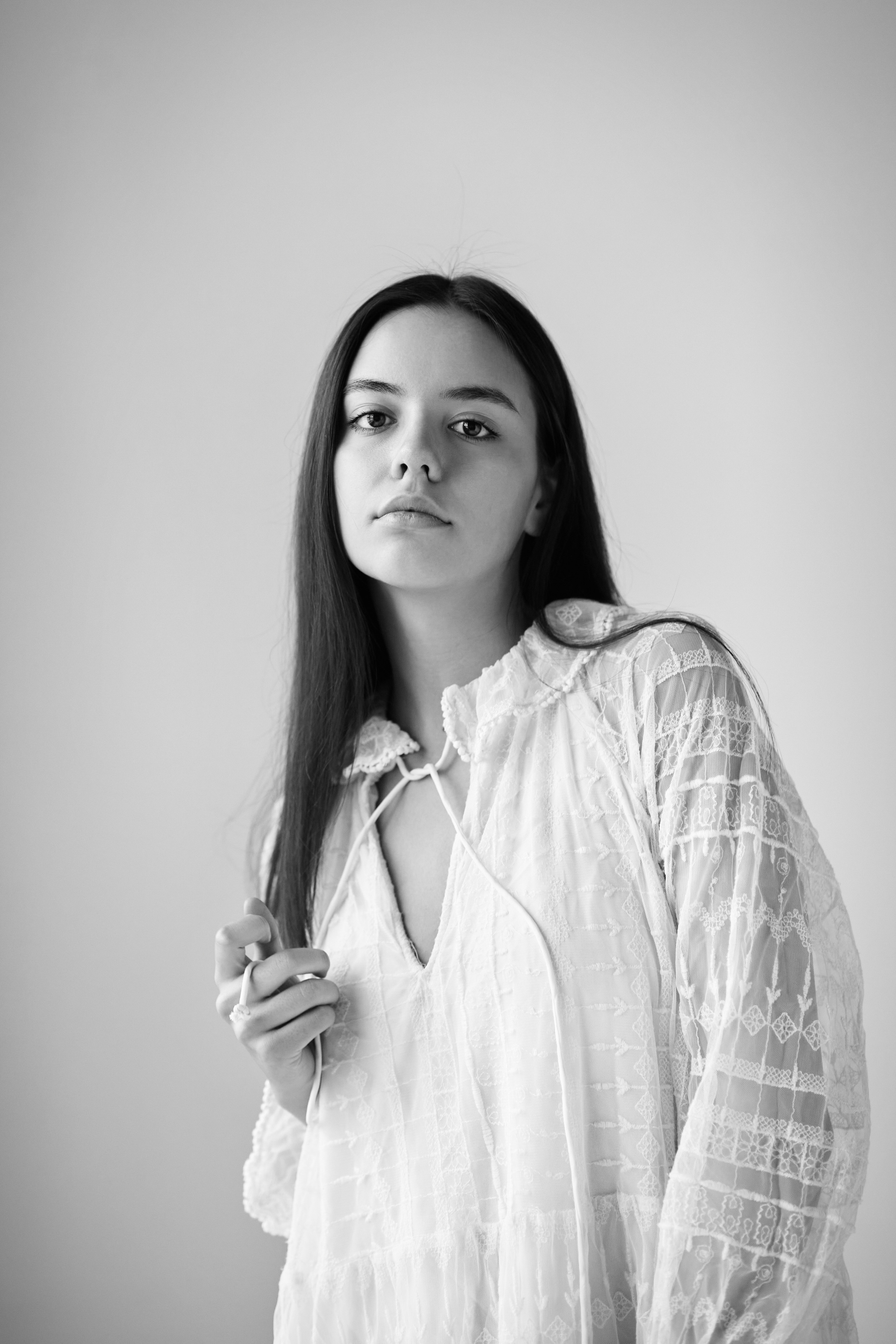 Модель Амина в топике стоит в студии на светлом фоне, ее волосы плавно обрамляют лицо.