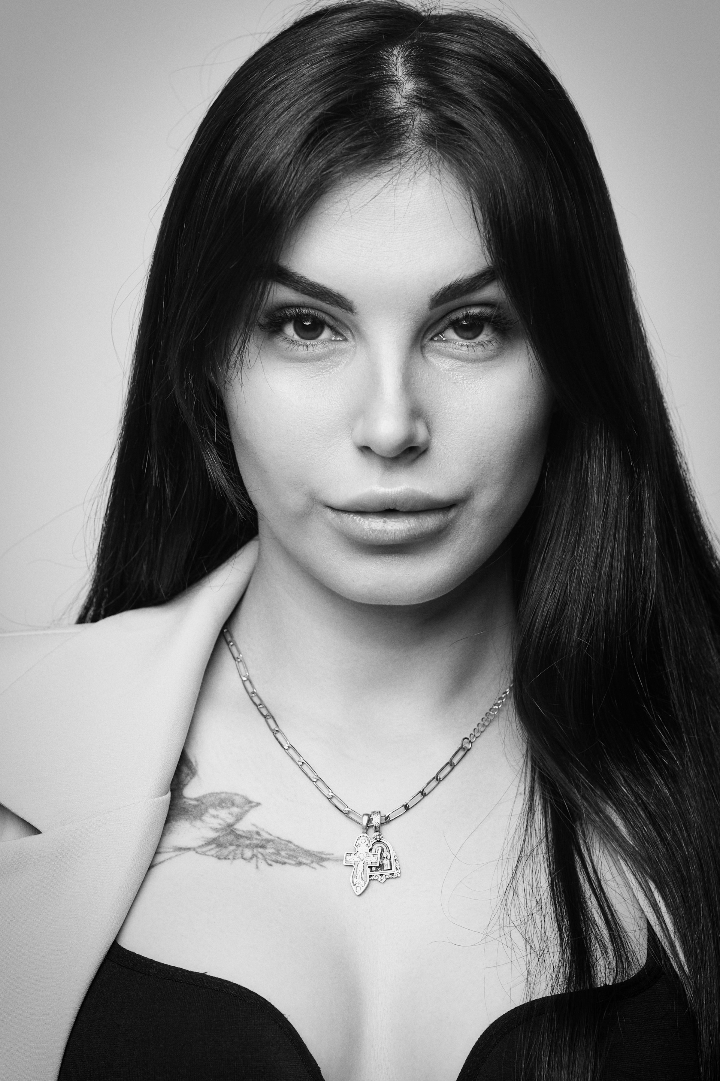 Карина выглядит элегантно в белой рубашке на светлом фоне в студии.