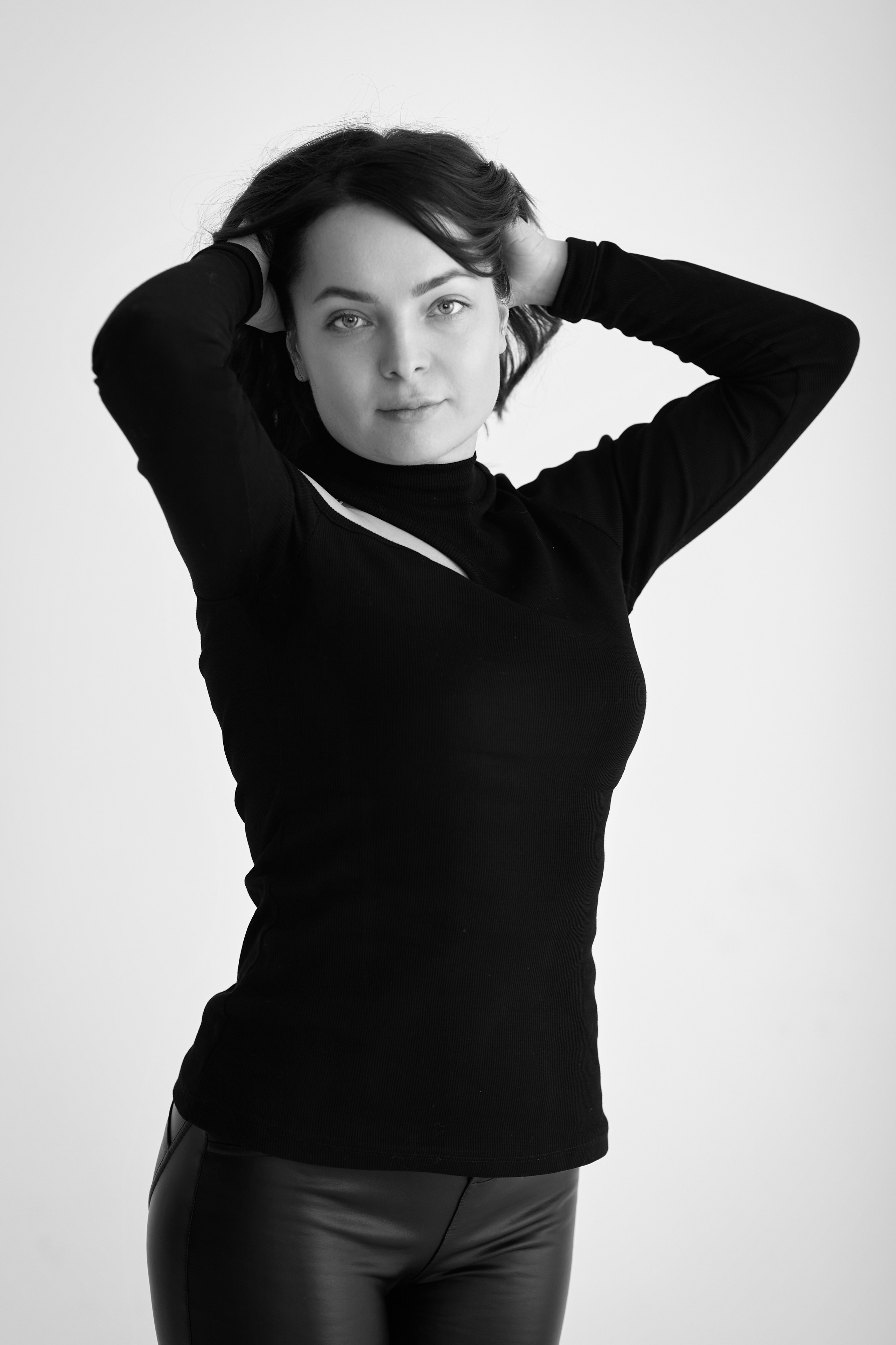 Темноволосая Татьяна, модель, сидит на стуле в студии на светлом фоне в светлом платье.