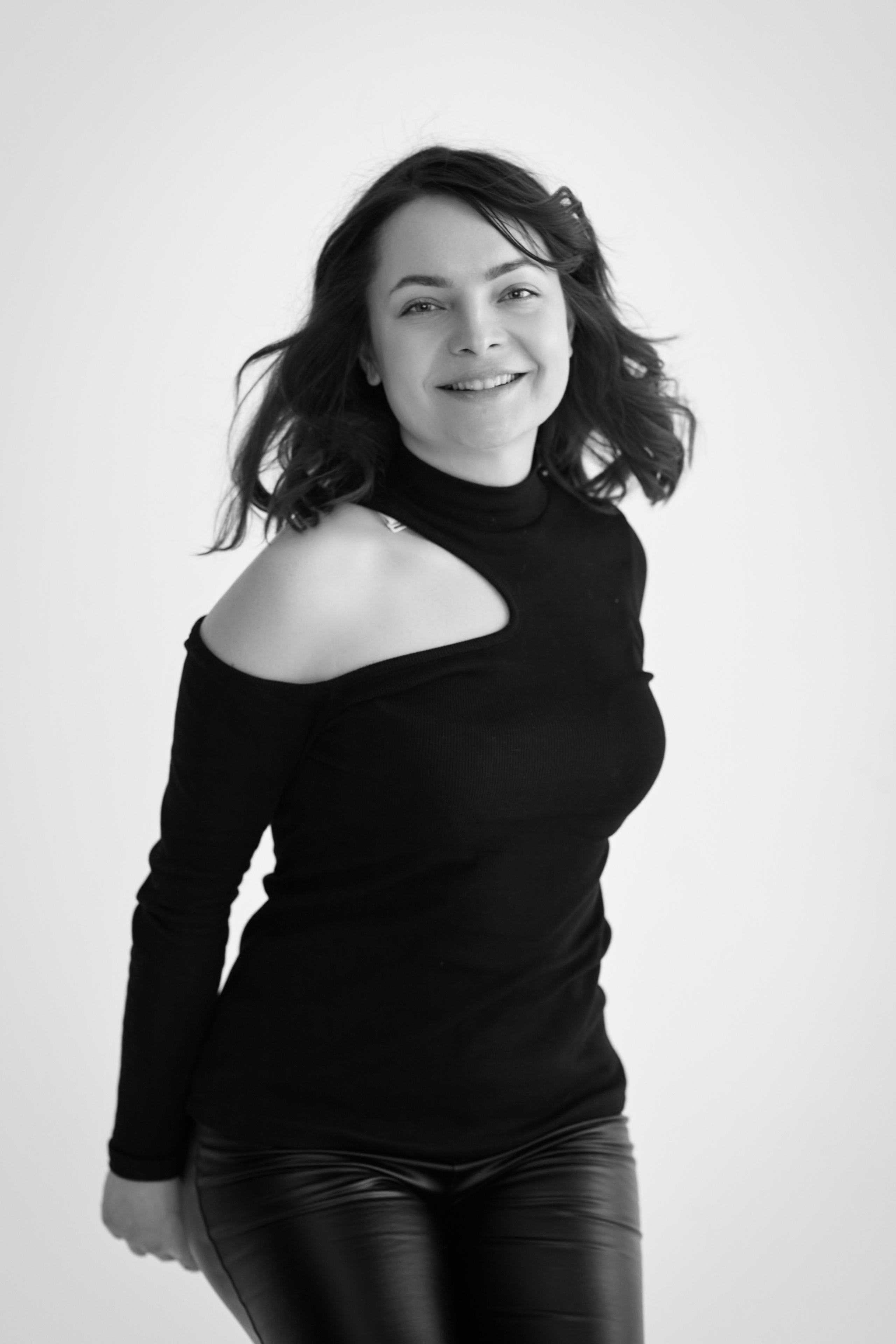 Темноволосая модель Татьяна находится на стуле в светлом топике на фоне светлой стены.