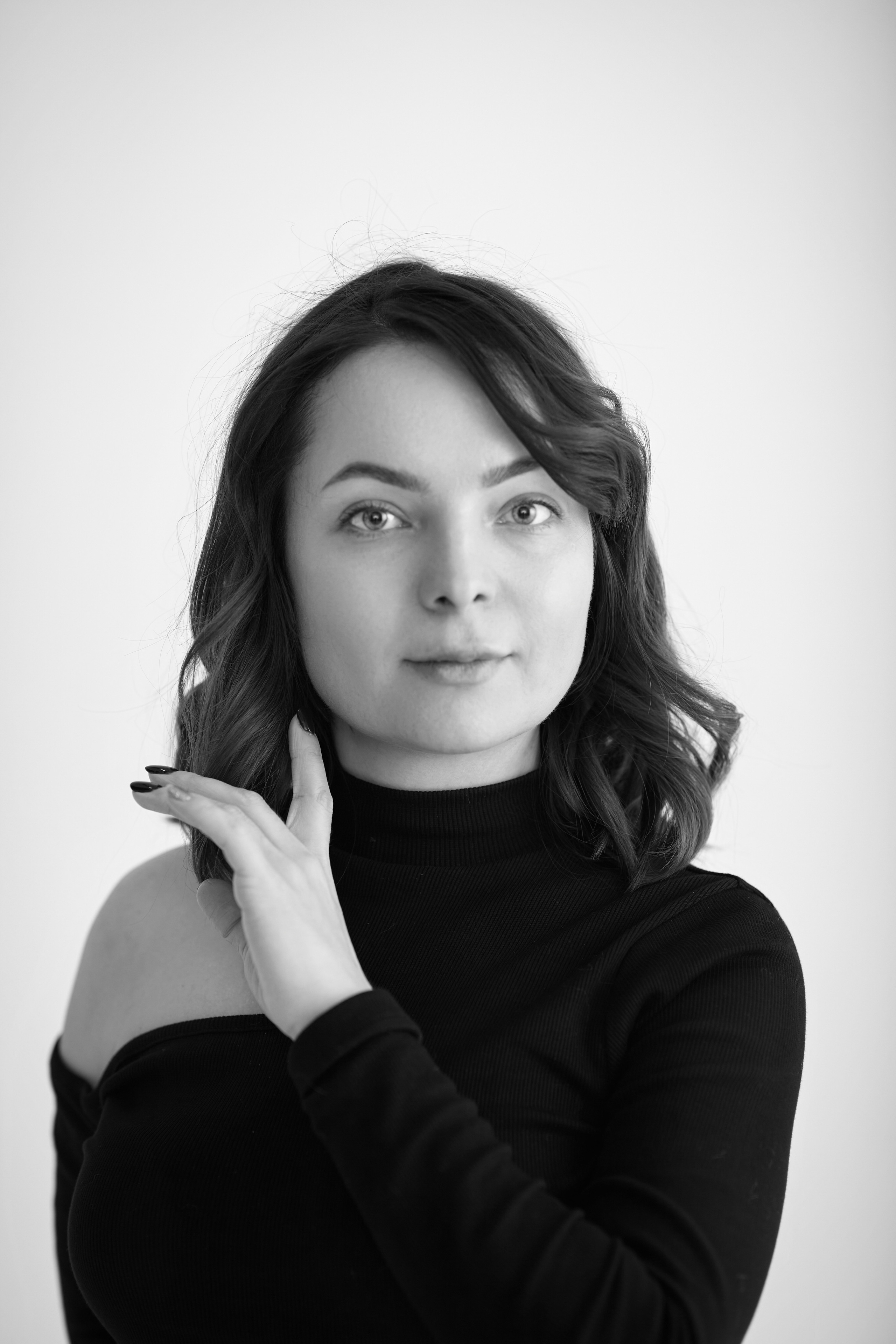 Темноволосая модель Татьяна стоит на светлом фоне в светлой рубашке в студии.