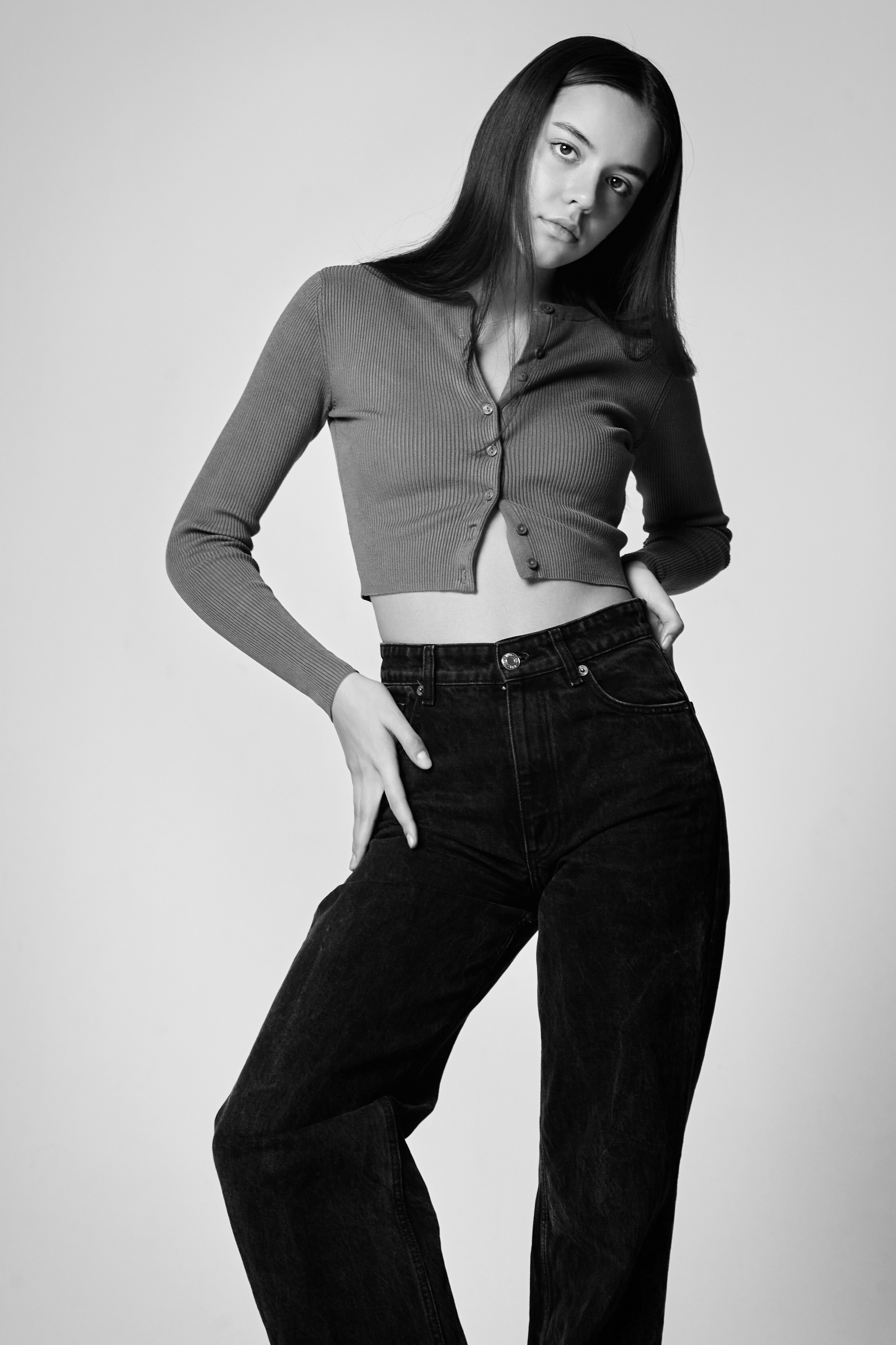 На светлом фоне темноволосая модель Амина в белом топике и черных леггинсах.