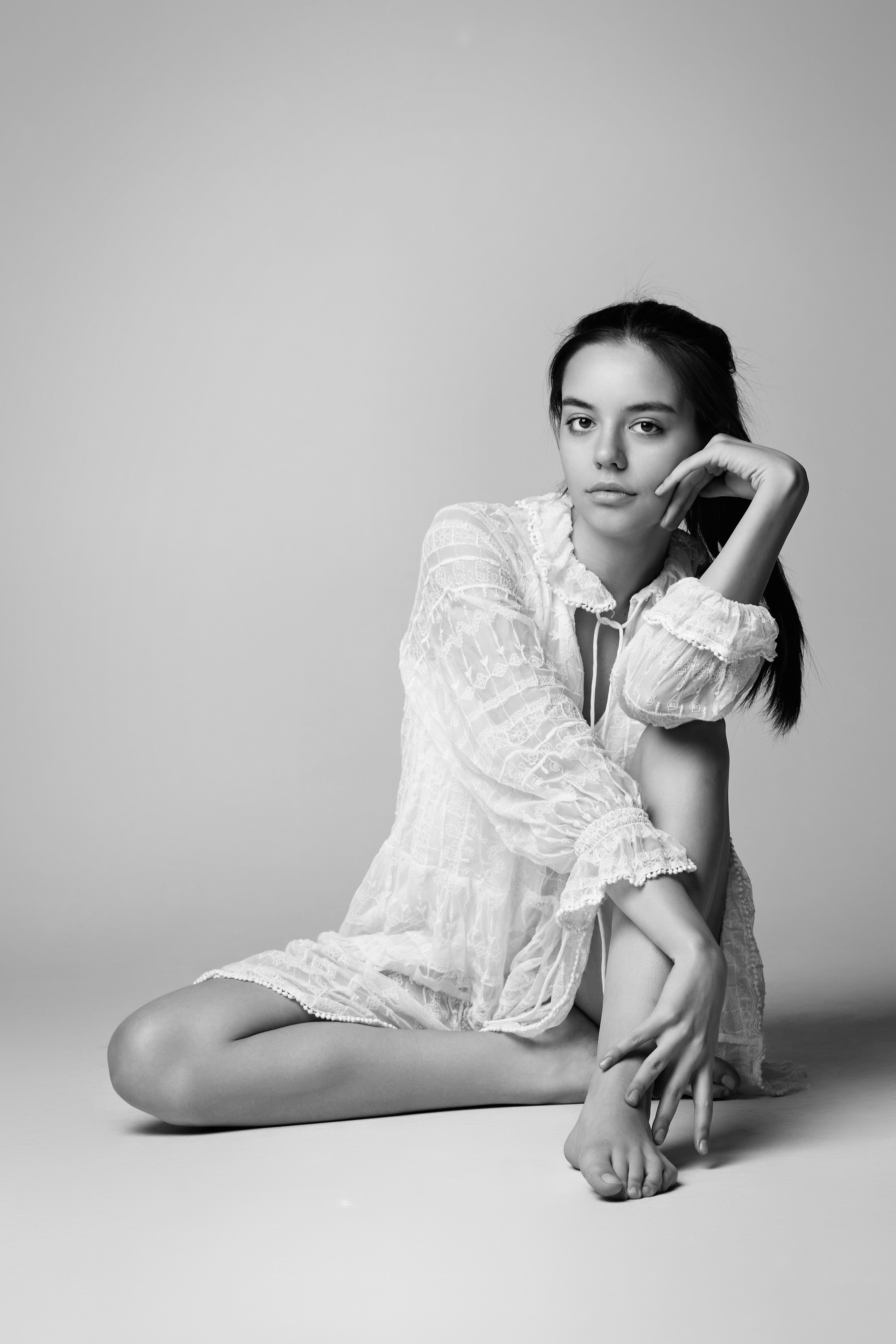 В студии на светлом фоне темноволосая модель Амина в светлом топике и джинсовых шортах.