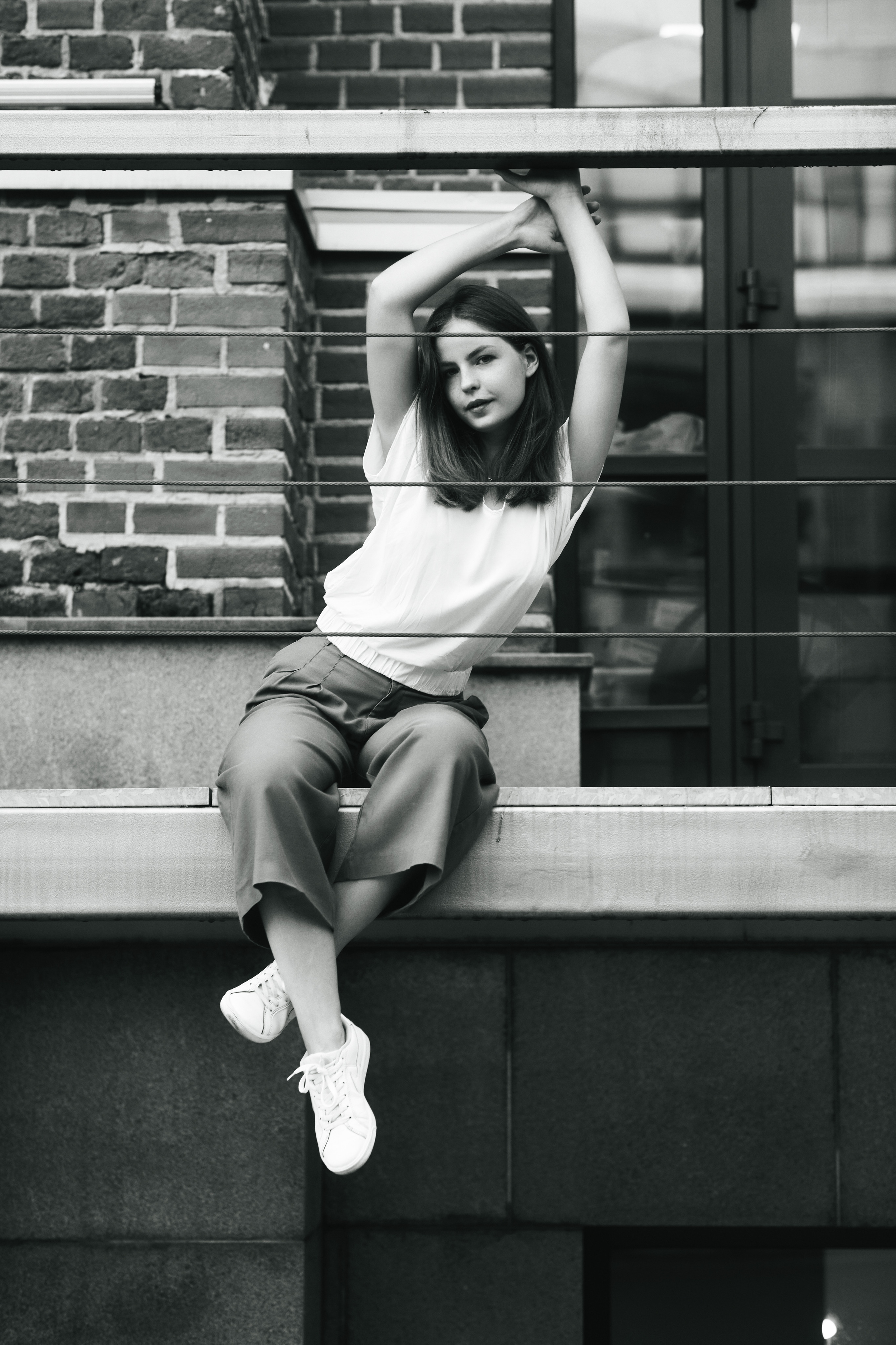 Дарья, модель с темными волосами, позирует на улице Москвы в белой кофте и широких брюках.