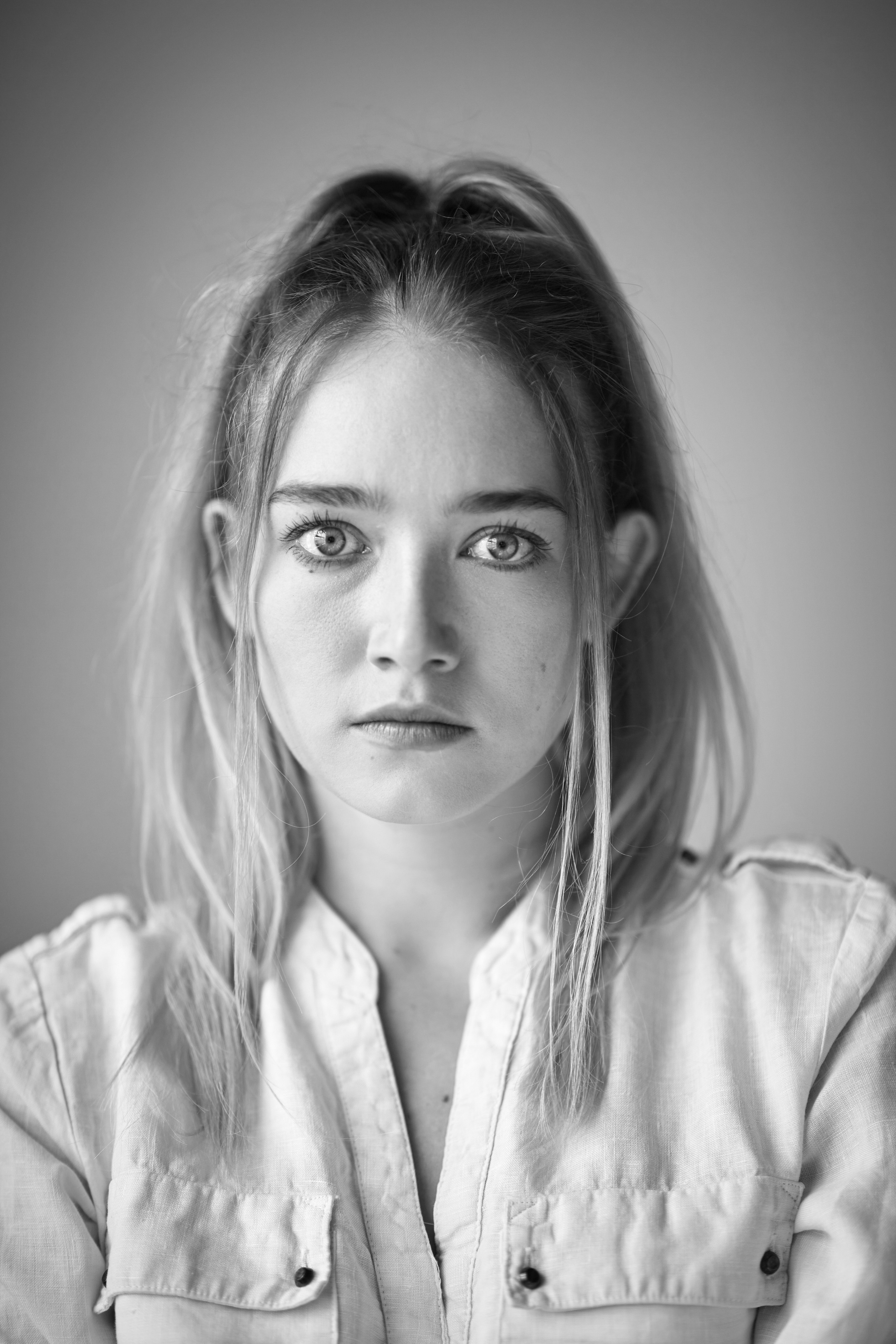 В своей белоснежной рубашке, светловолосая модель Алиса выглядит красиво на светлом фоне студии.
