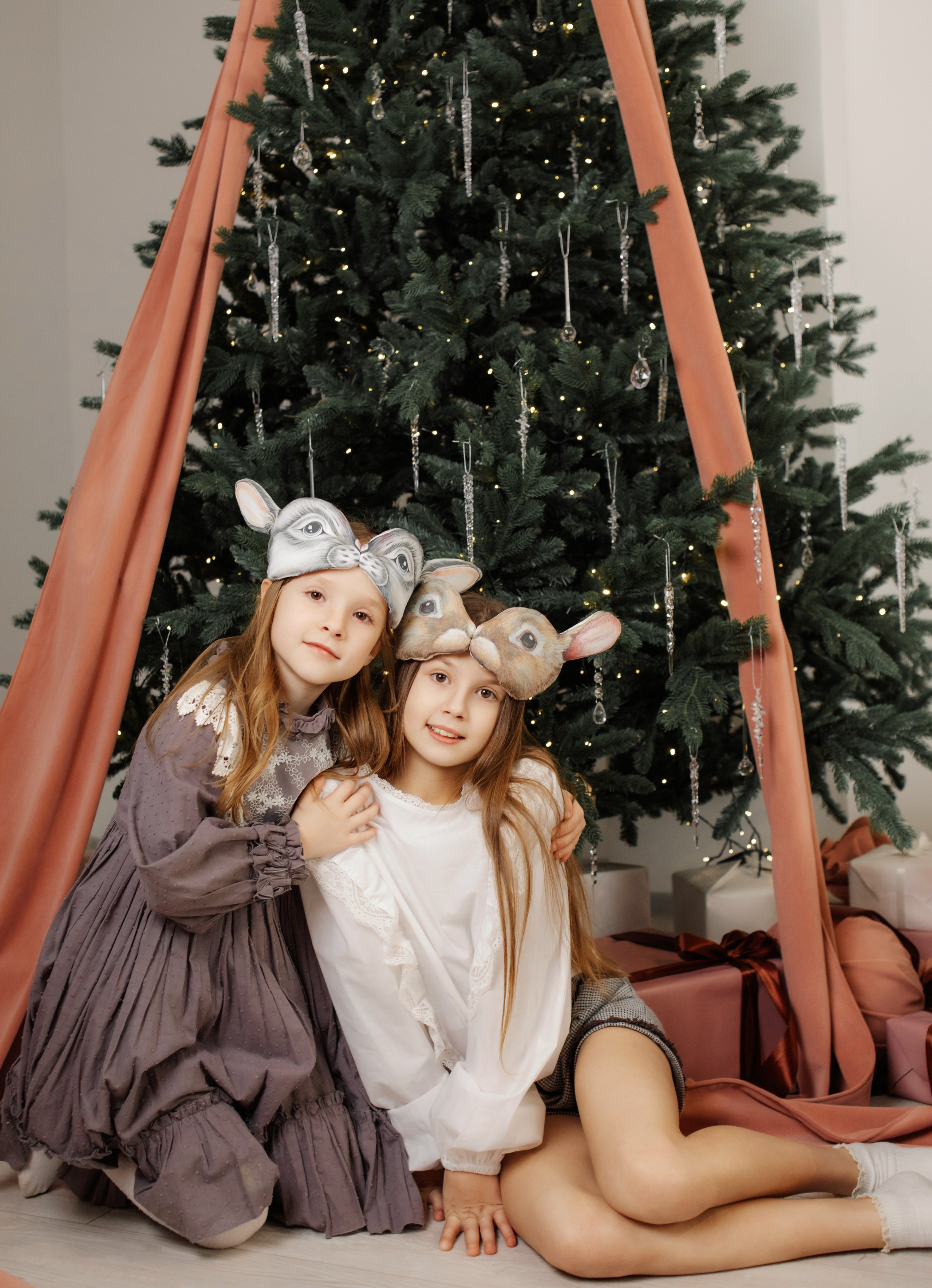 Сестры в студии у елки в красивых платьях и масках зверей