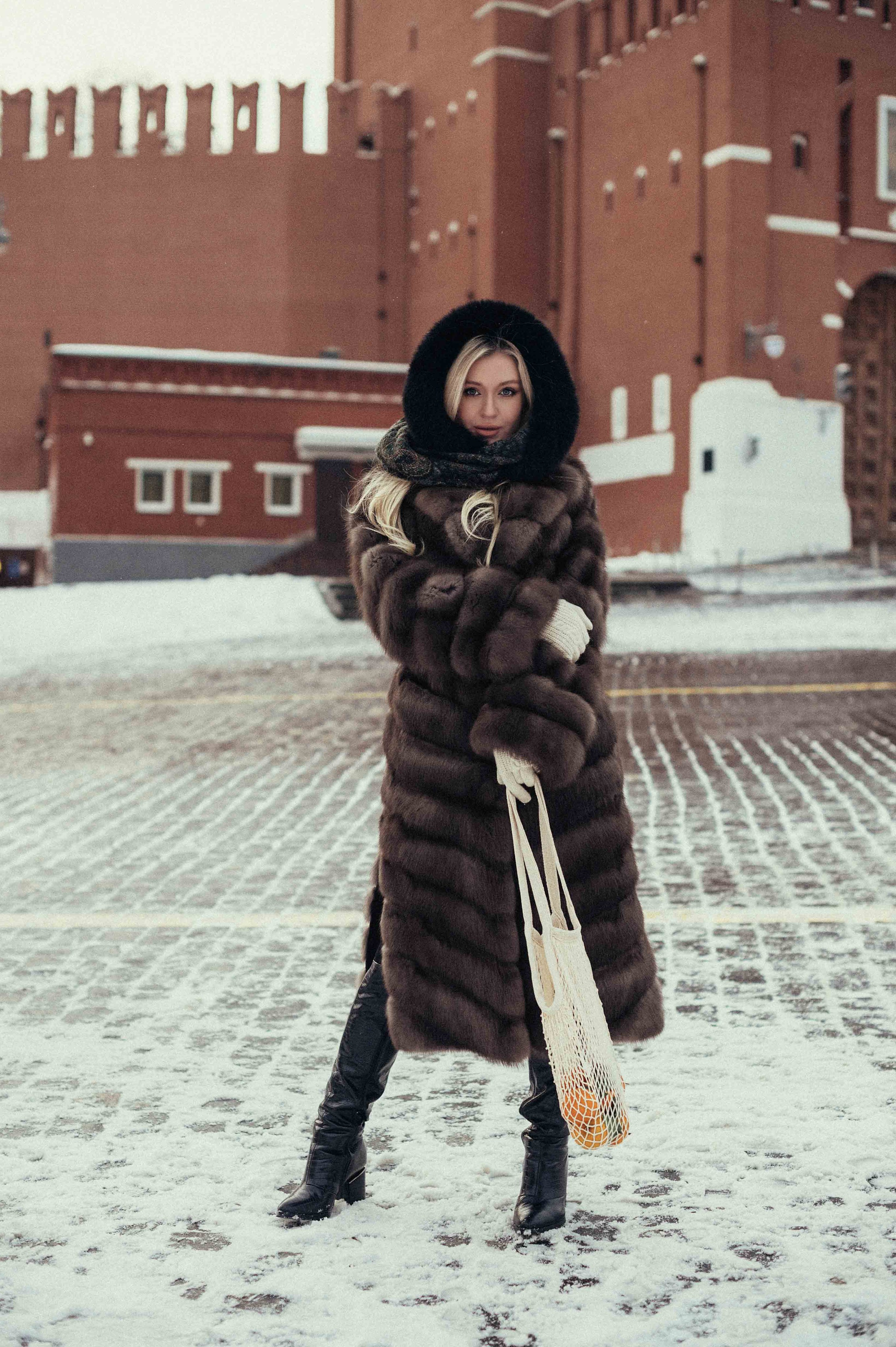 Фотосессия в стиле Russian girl на Красной площади на фоне Спасской башни Кремля, на которой девушка стоит в соболиной шубе, держа авоську мандаринов в руках