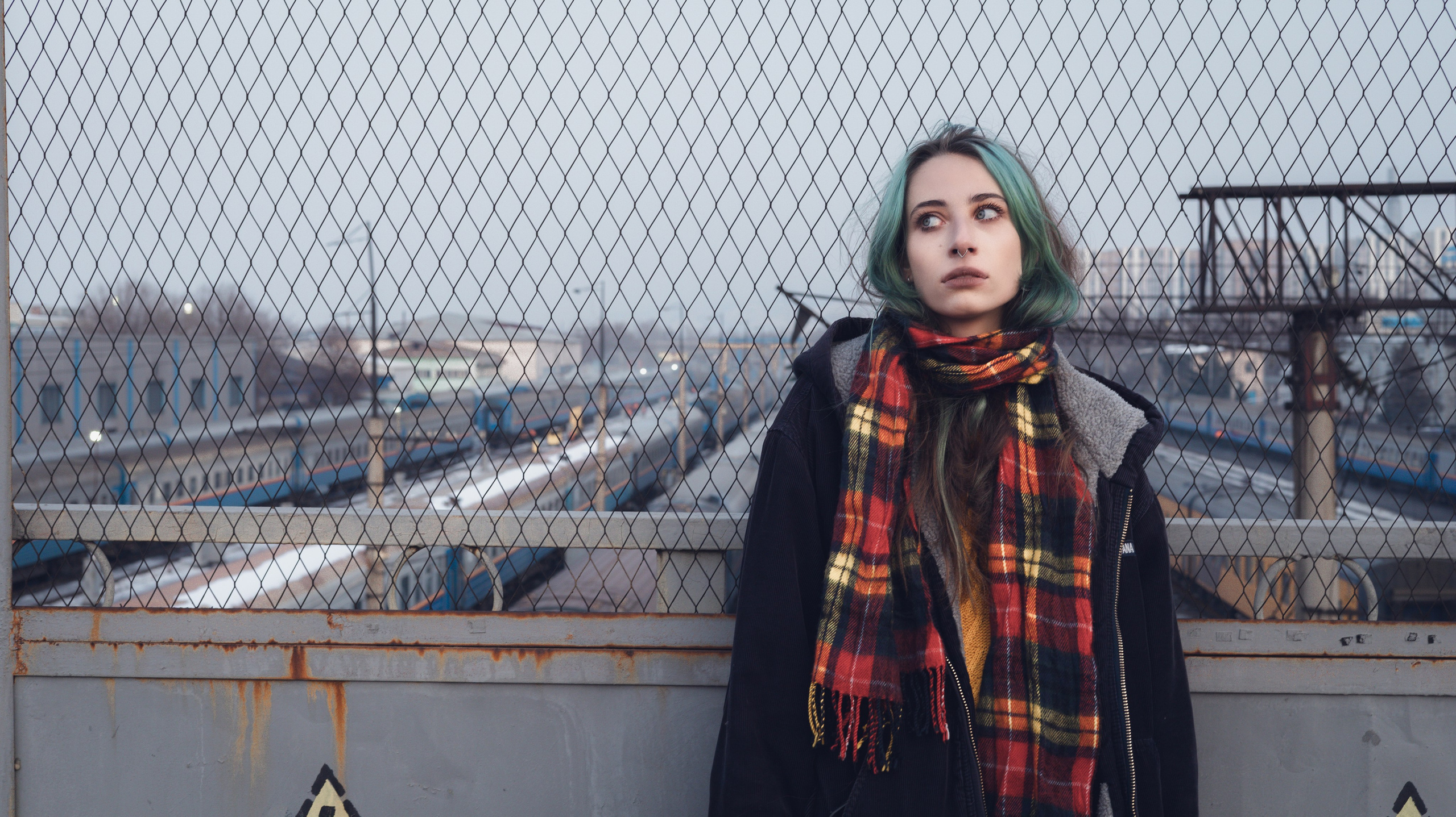 Девушка стоит у забора в лучах заката, взгляд в сторону