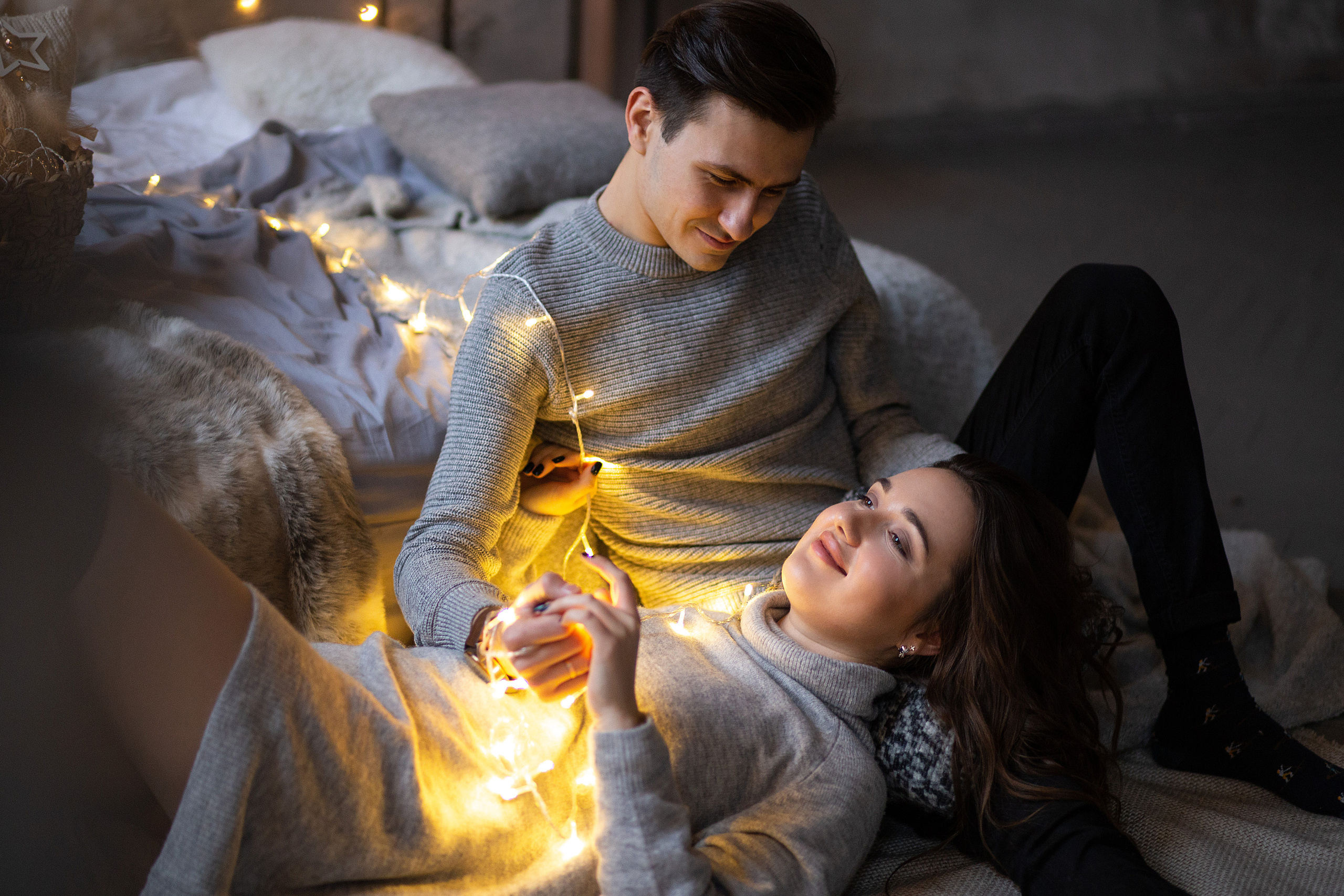 девушка  и молодой человек  лежат на  полу. они  обмотаны  гирляндой